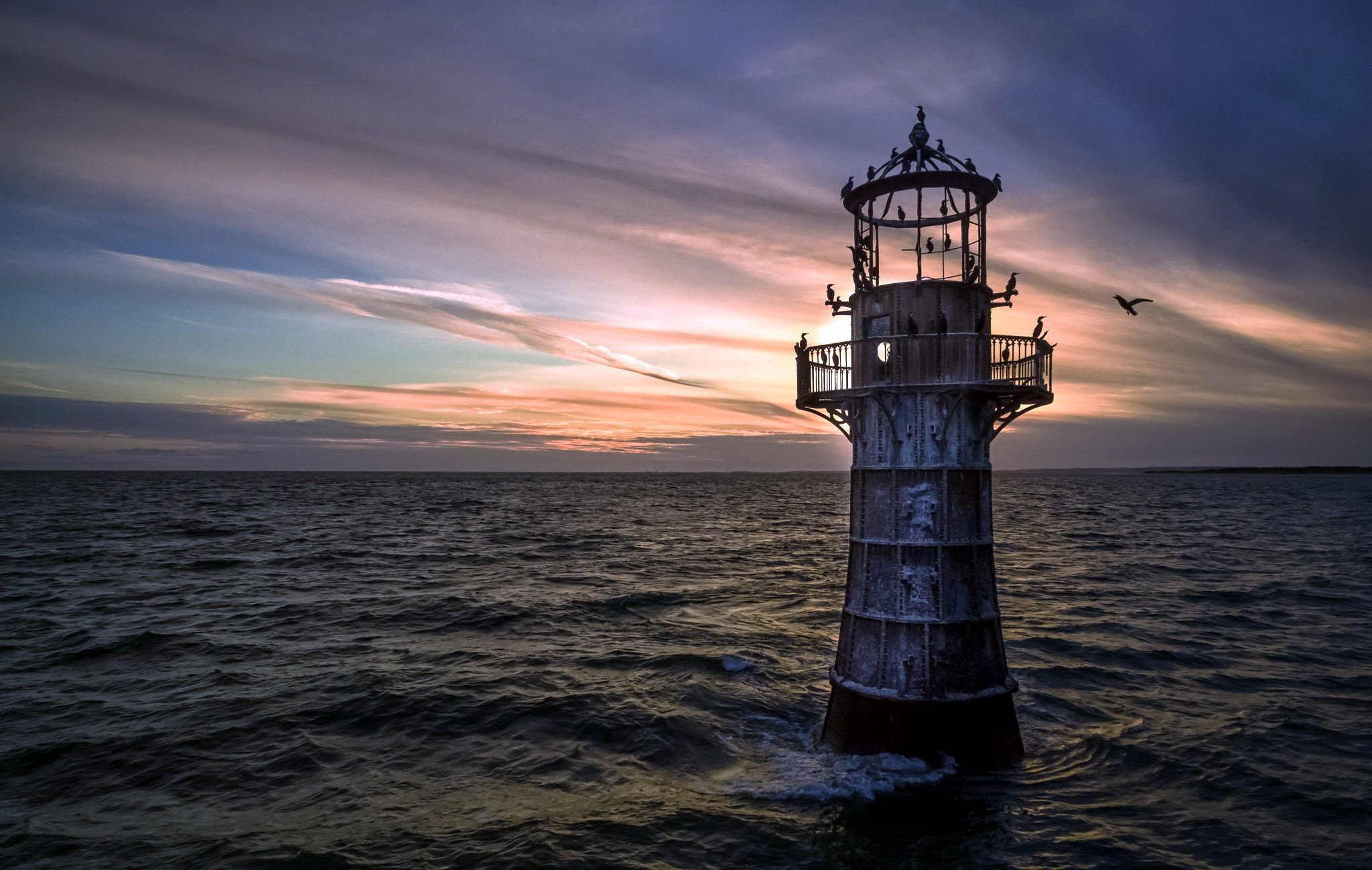 Lighthouse in the sea at sunset with birds HD Wallpaper