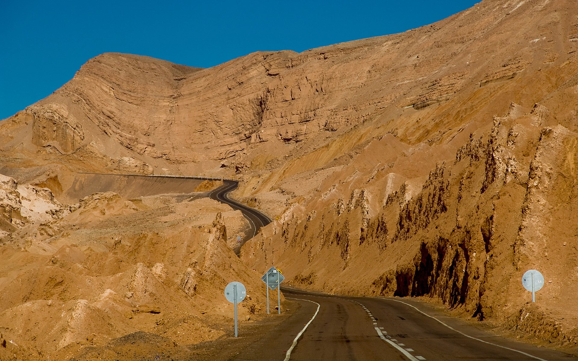Desert road winding through arid mountains HD Wallpaper