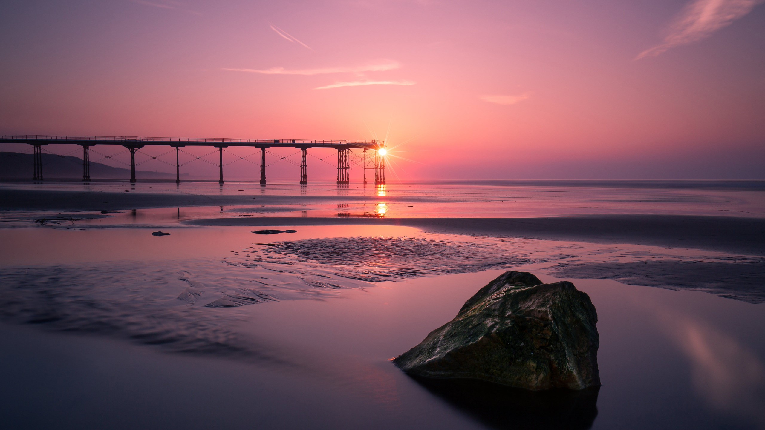 Sunset over a pier and beach with a rock HD Wallpaper