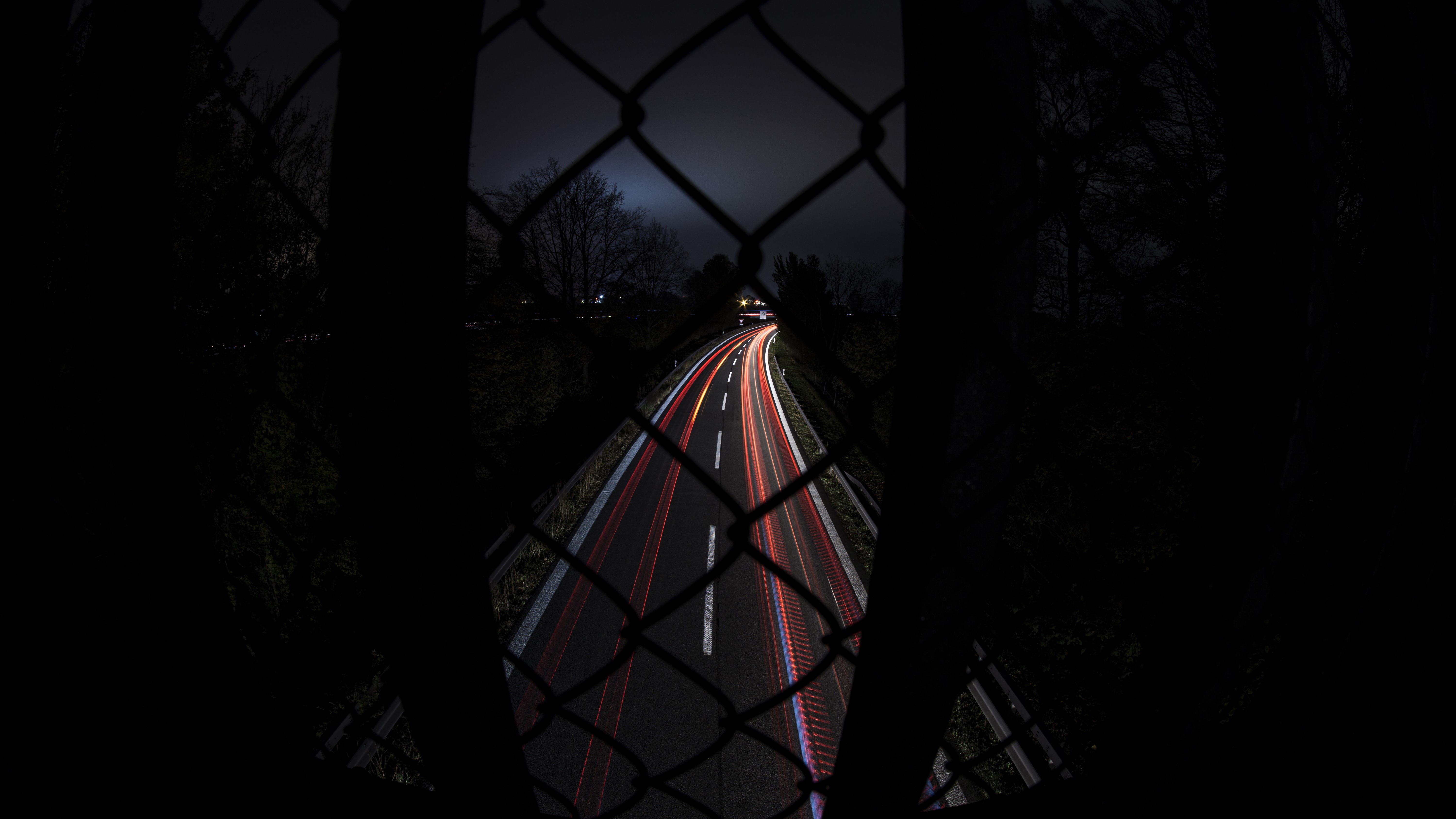 4K long exposure of a highway at night through a fence HD Wallpaper