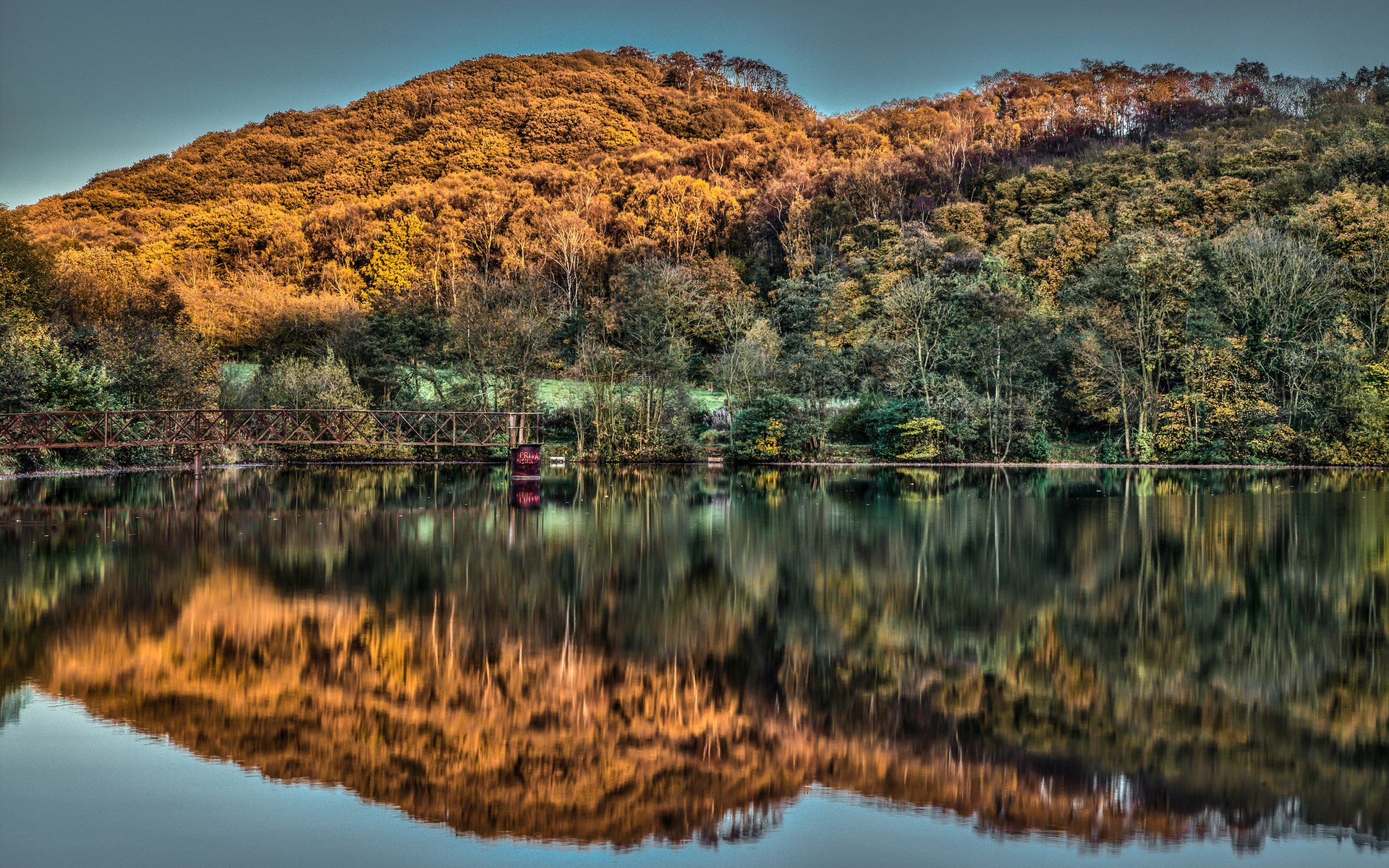 Autumn forest reflected in a lake with a bridge HD Wallpaper