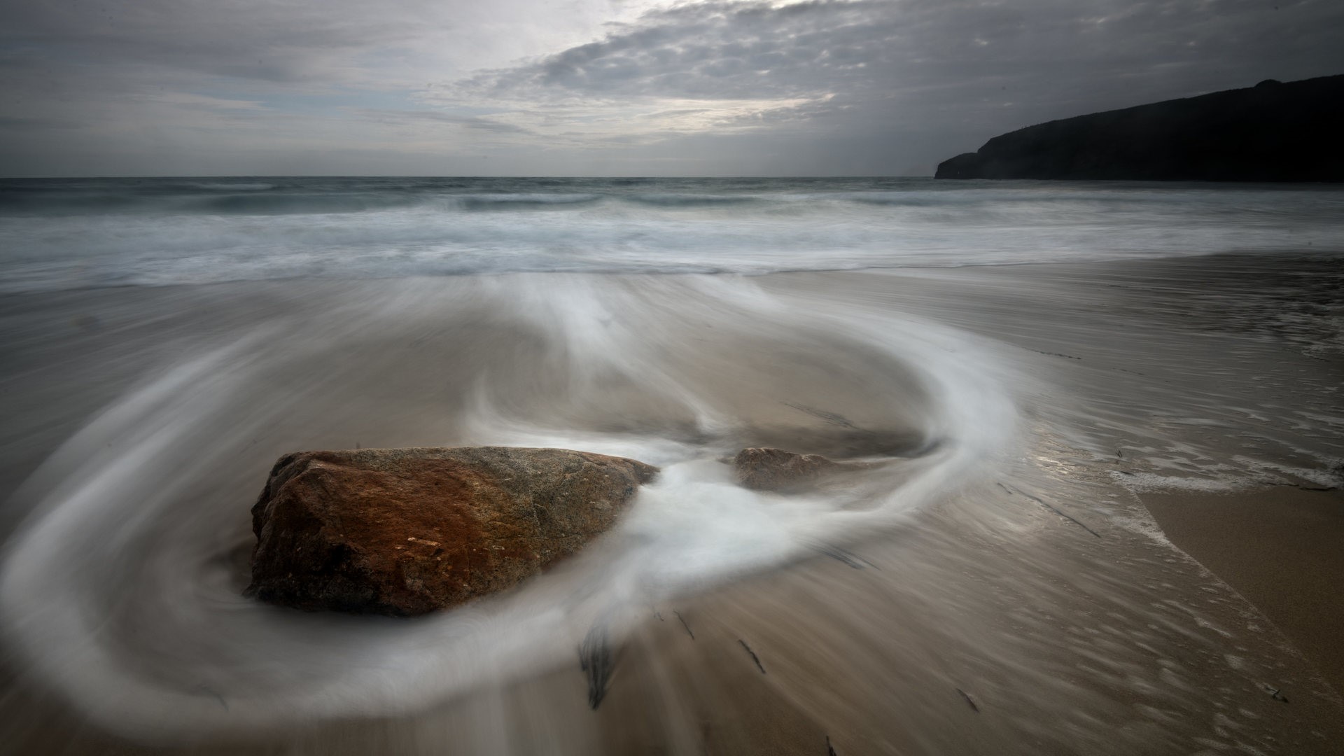 Long exposure of waves swirling around rocks on a beach HD Wallpaper