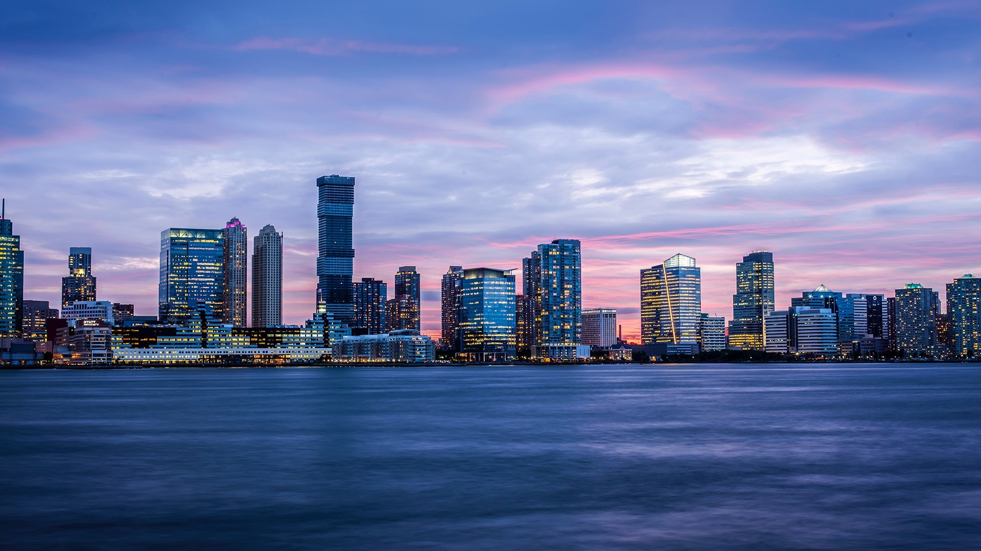 City skyline at dusk with purple clouds and water HD Wallpaper