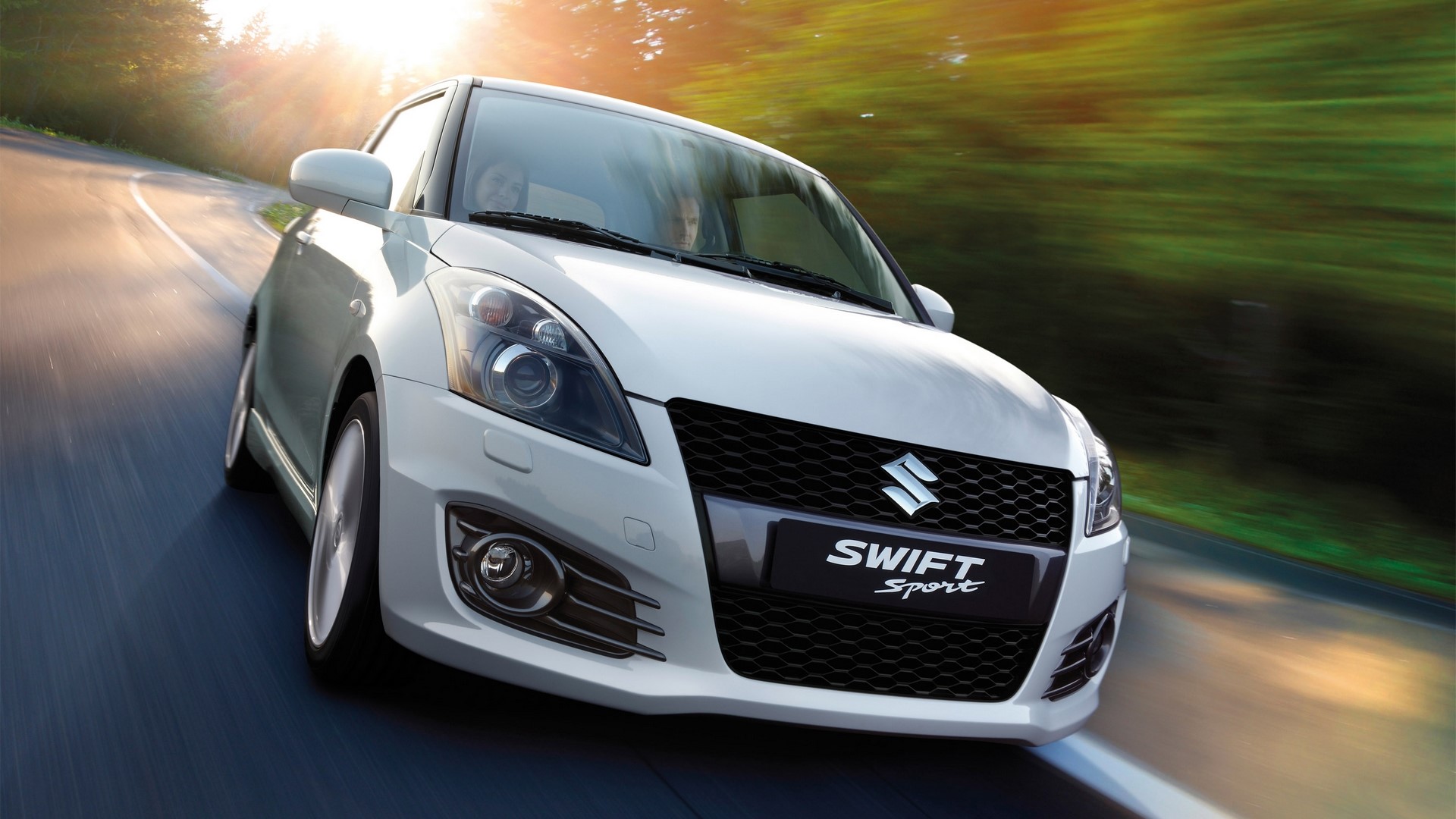 White Suzuki Swift Sport driving on a winding road HD Wallpaper