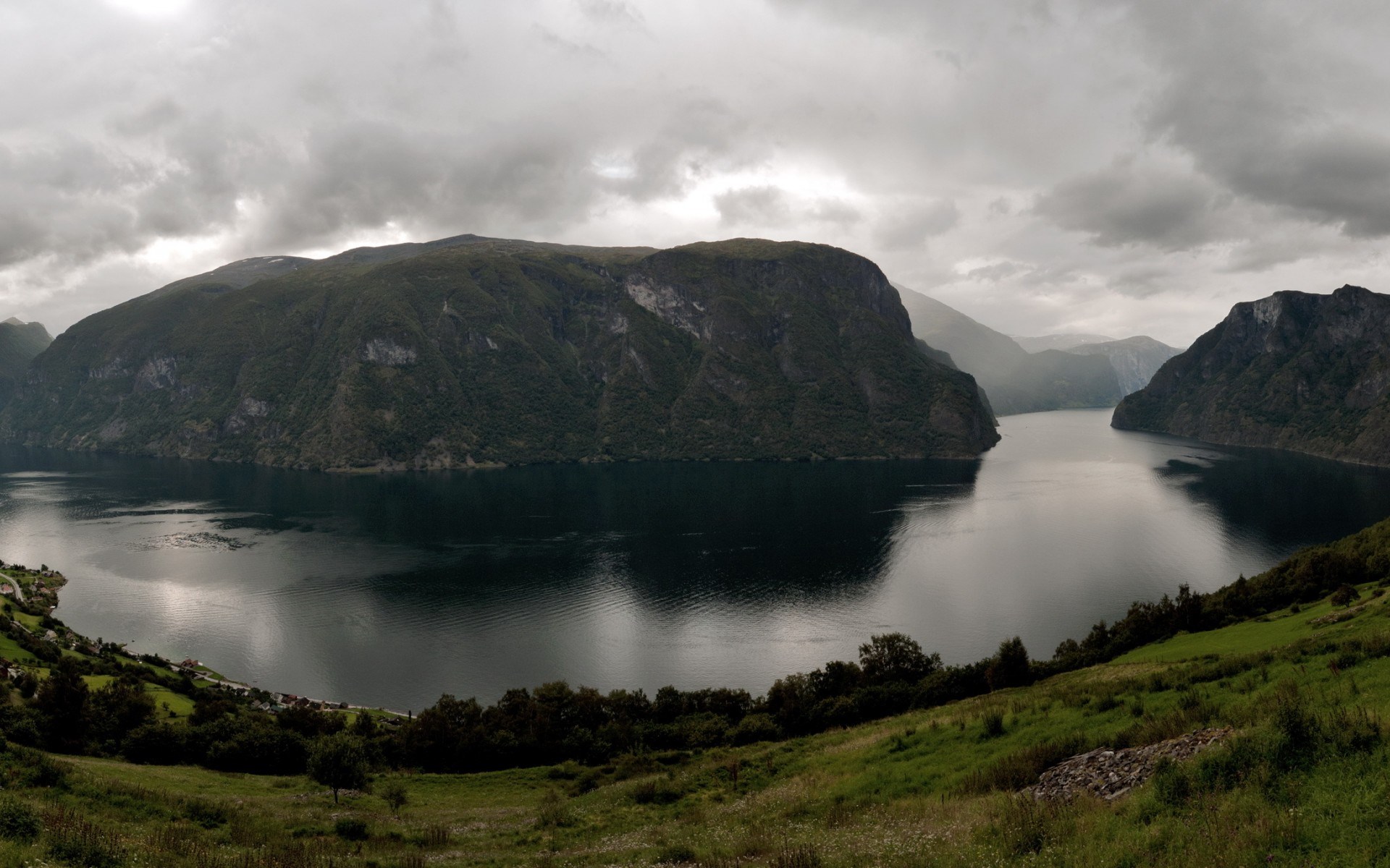 Panoramic view of a fjord with steep, tree-covered mountains under a cloudy sky HD Wallpaper