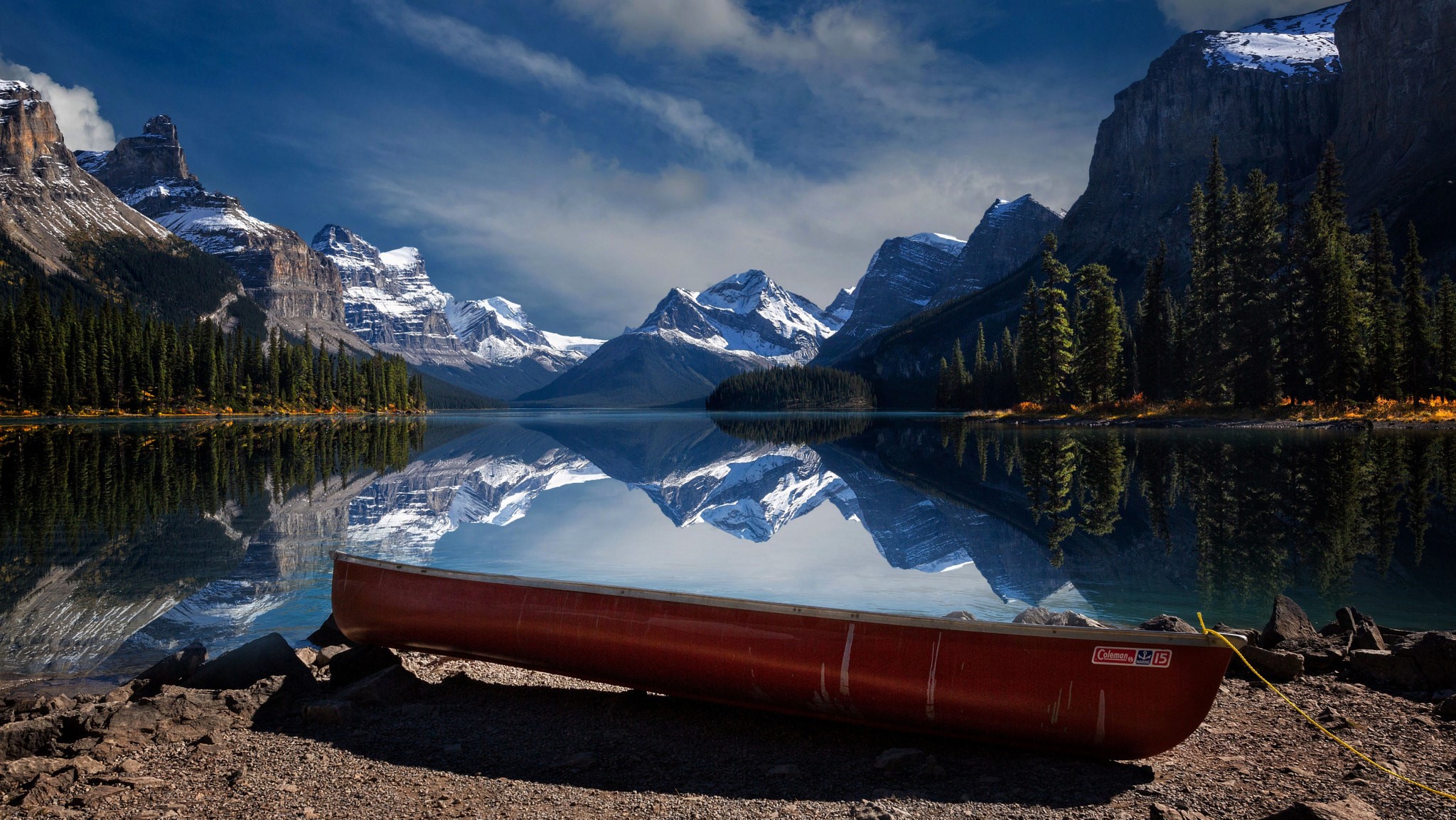 Canoe on a rocky shore with snow-capped mountains and lake reflection HD Wallpaper