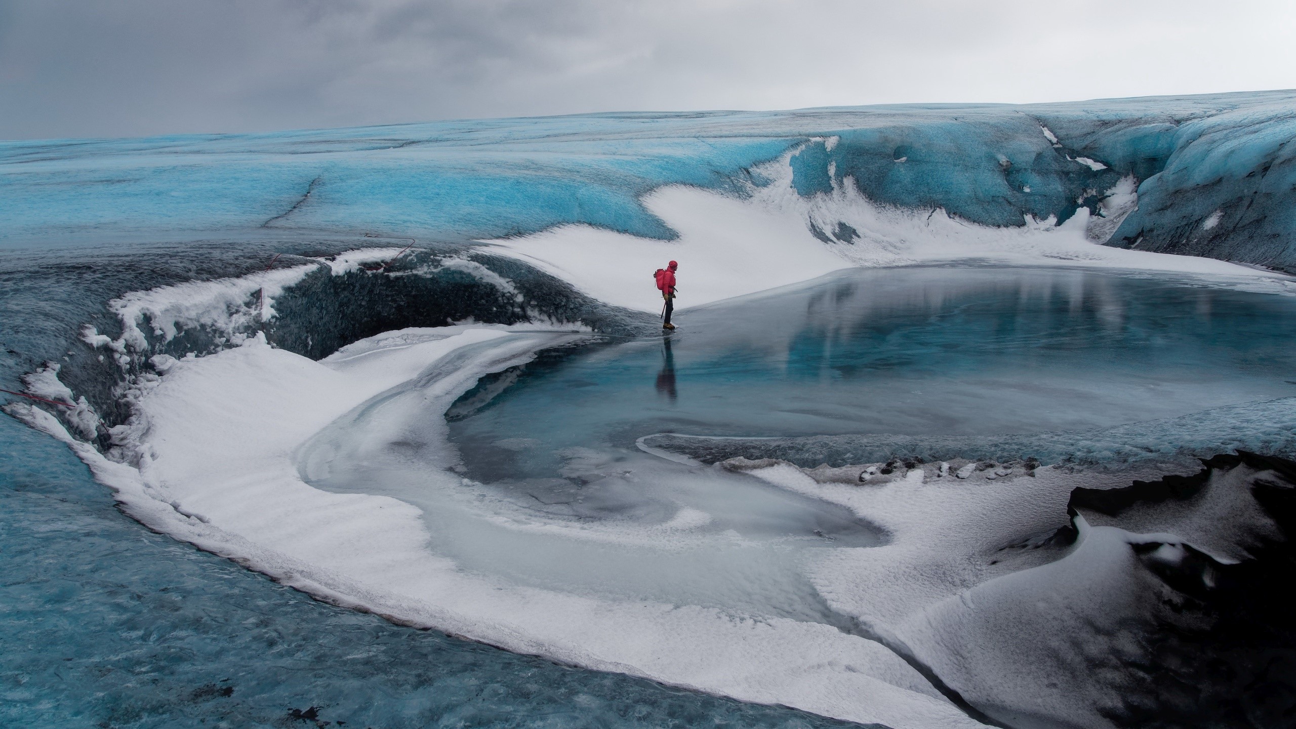Person on a glacier with a blue ice lake HD Wallpaper