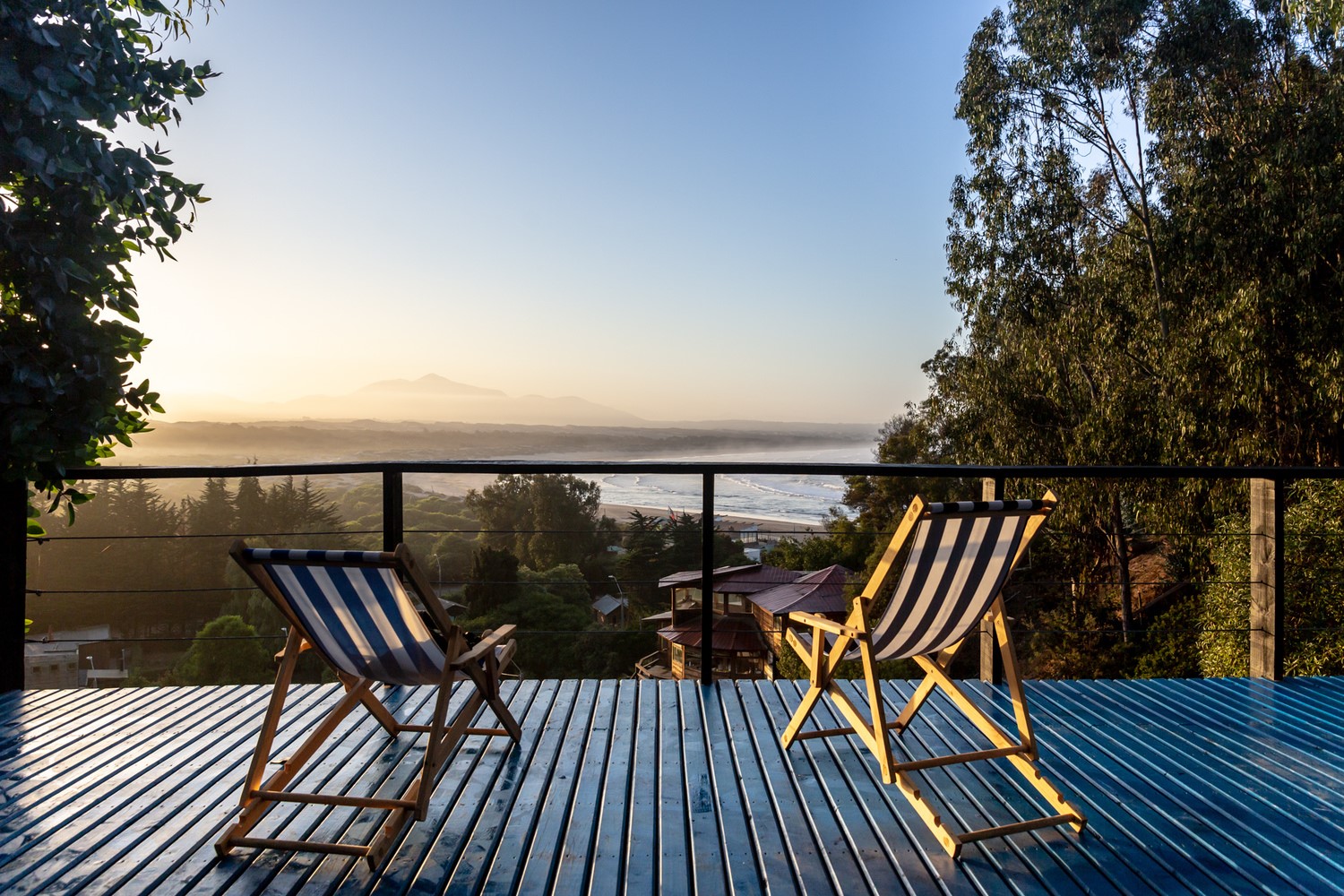 Deck chairs on a wooden deck overlooking the ocean at sunrise HD Wallpaper