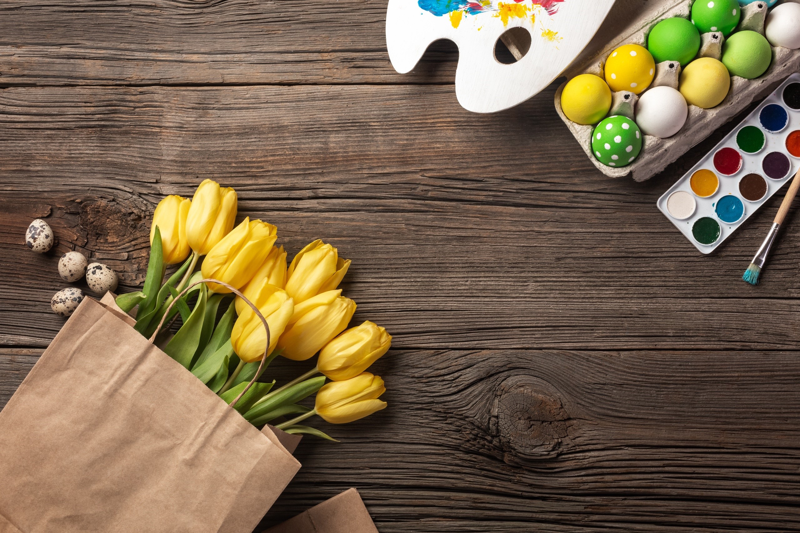 Easter eggs, tulips, and painting supplies on wooden table HD Wallpaper