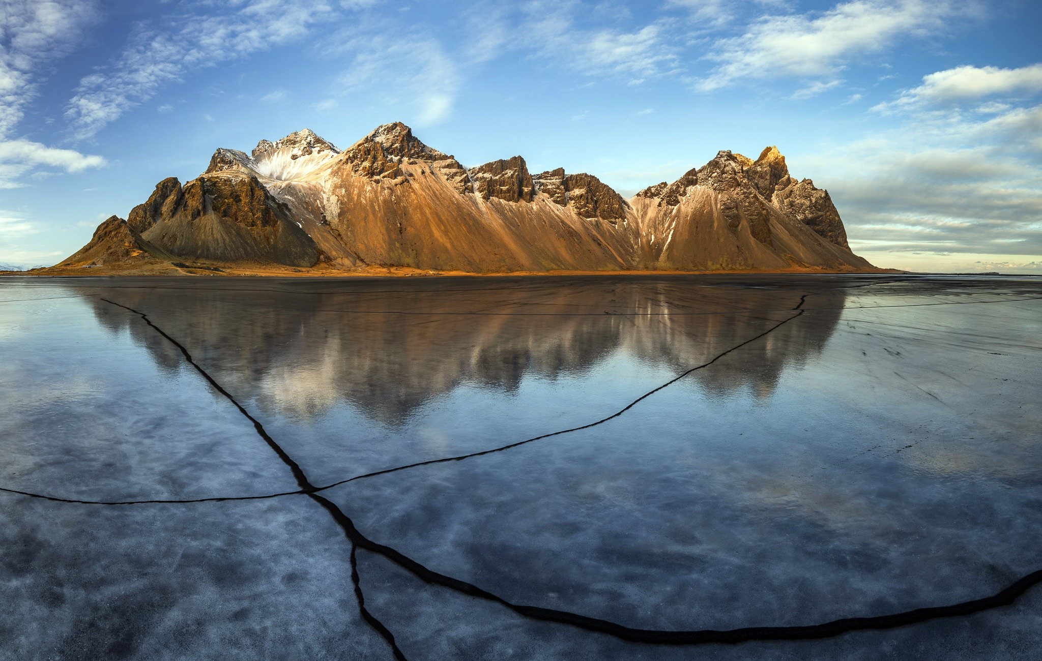 Jagged mountains reflected in cracked ice under a cloudy sky HD Wallpaper