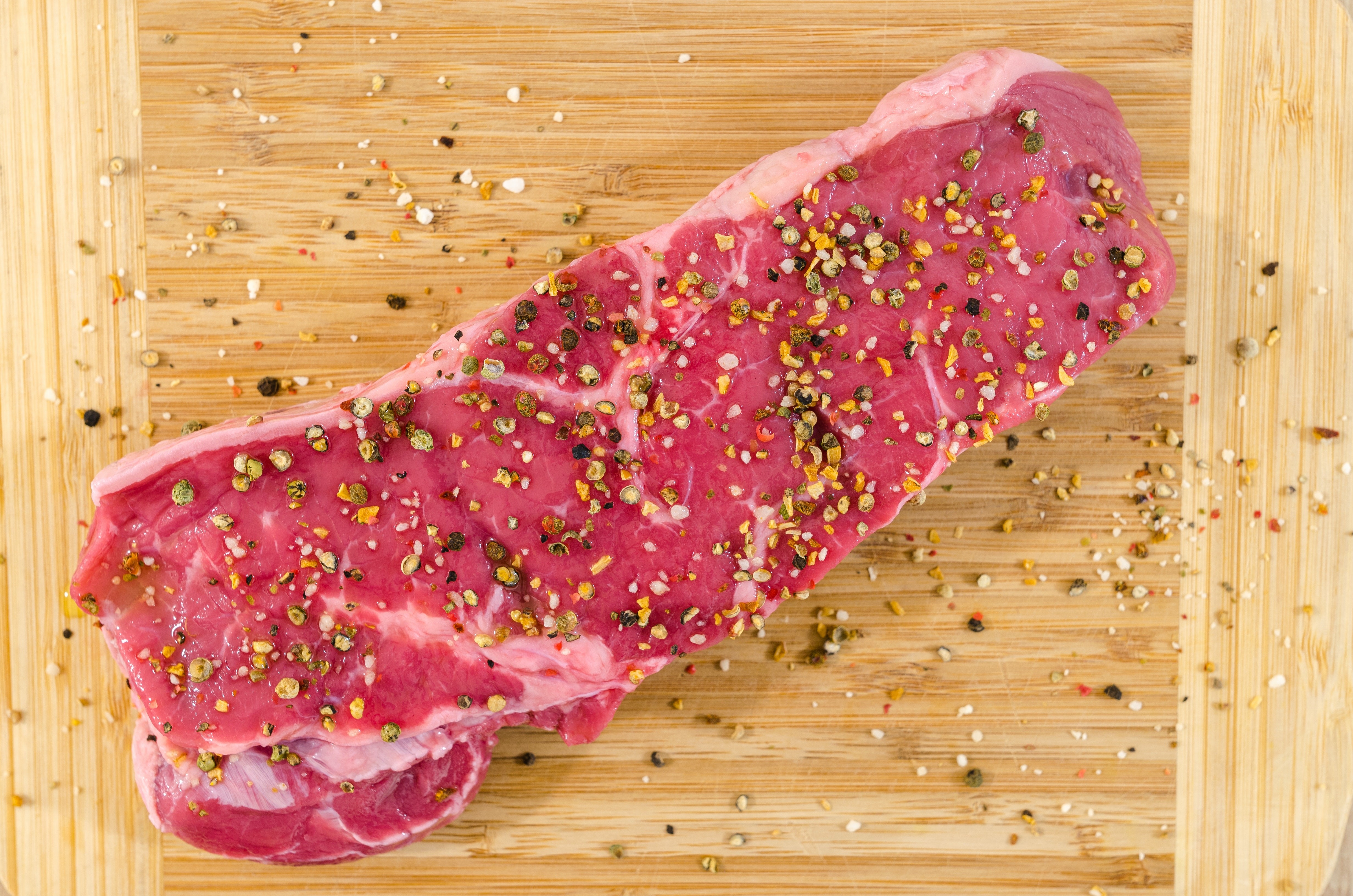 Raw beef steak seasoned with pepper and spices on a cutting board HD Wallpaper