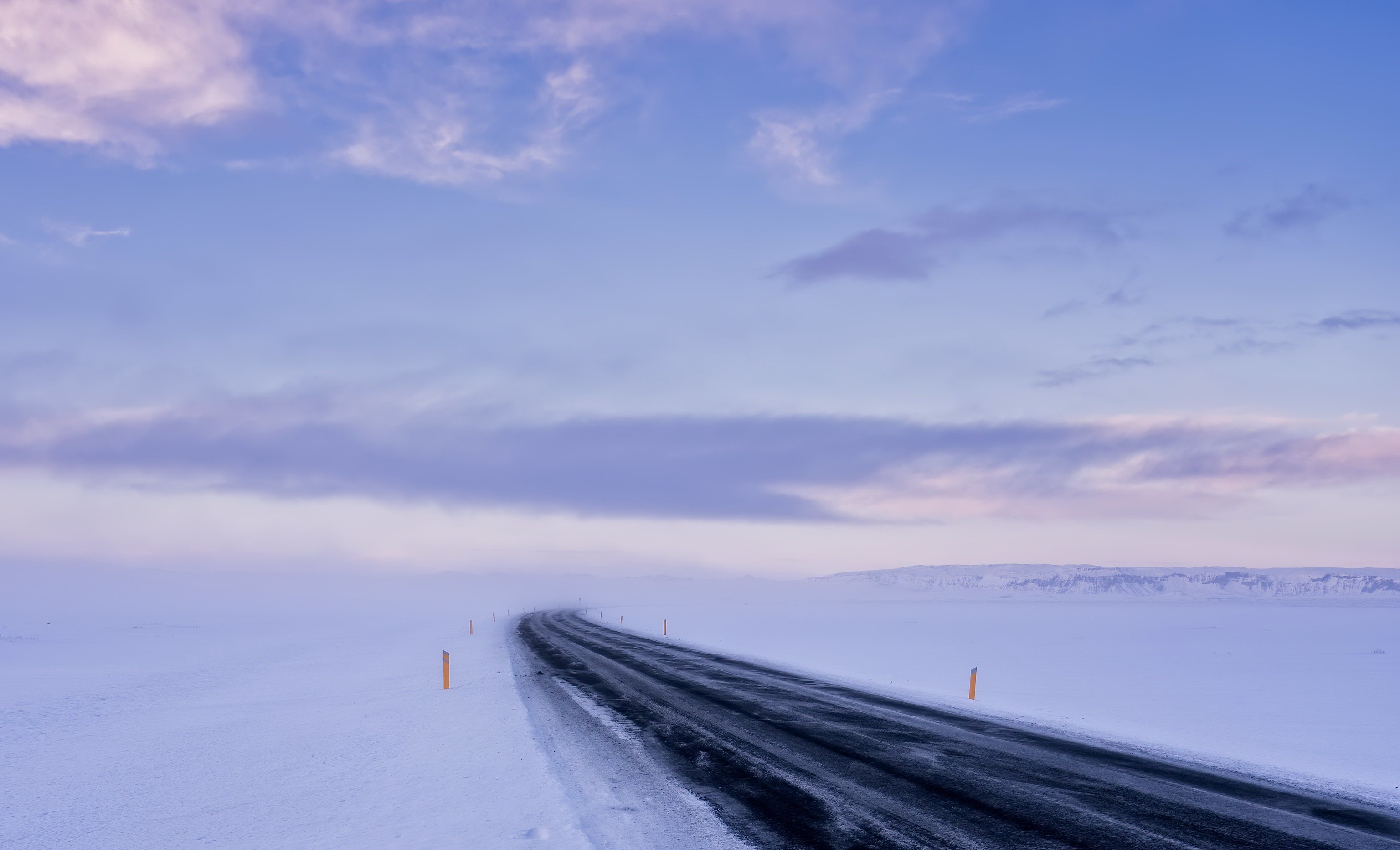 A lonely road through a snowy landscape under a cloudy sky HD Wallpaper