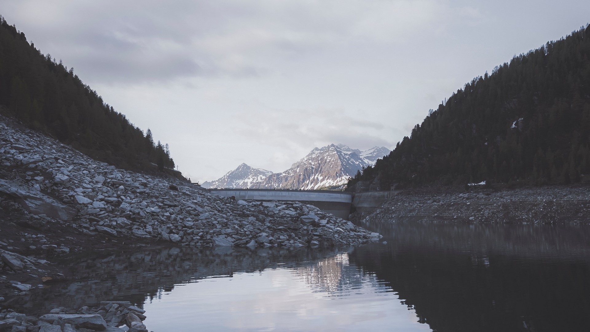 Snowy mountains behind a dam and lake HD Wallpaper