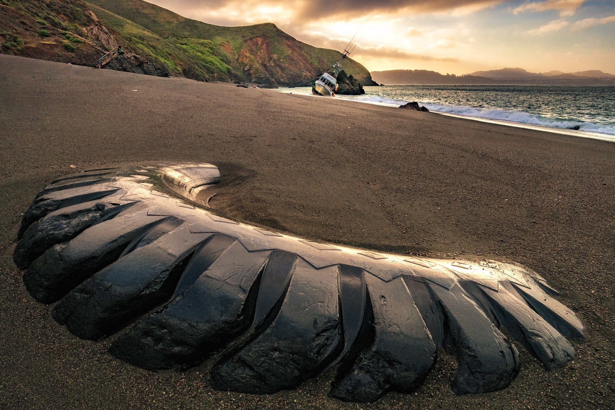 Wrecked boat and large tire on a sandy beach HD Wallpaper