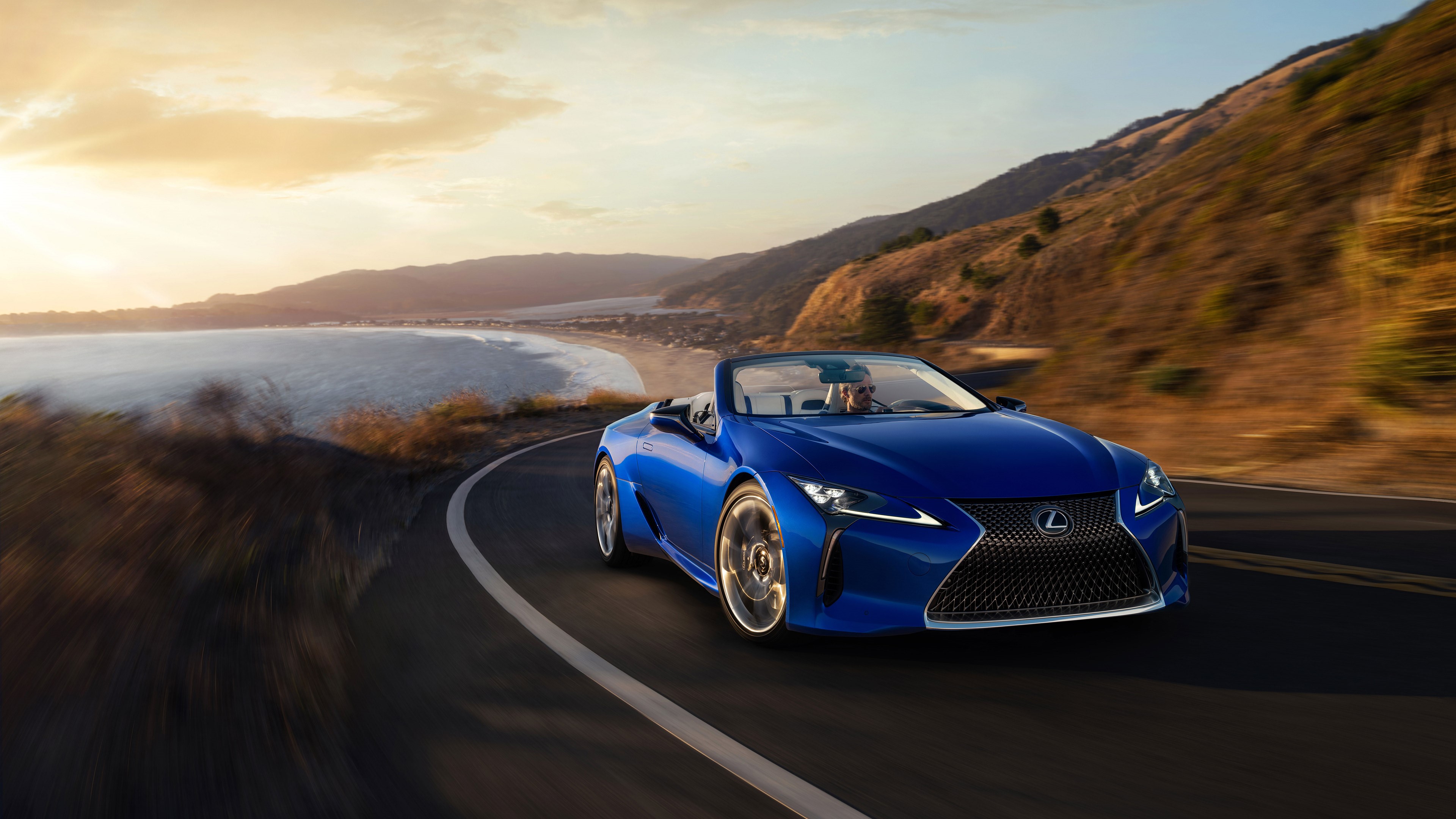 Blue Lexus LC-500 Convertible driving on coastal road at sunset HD Wallpaper
