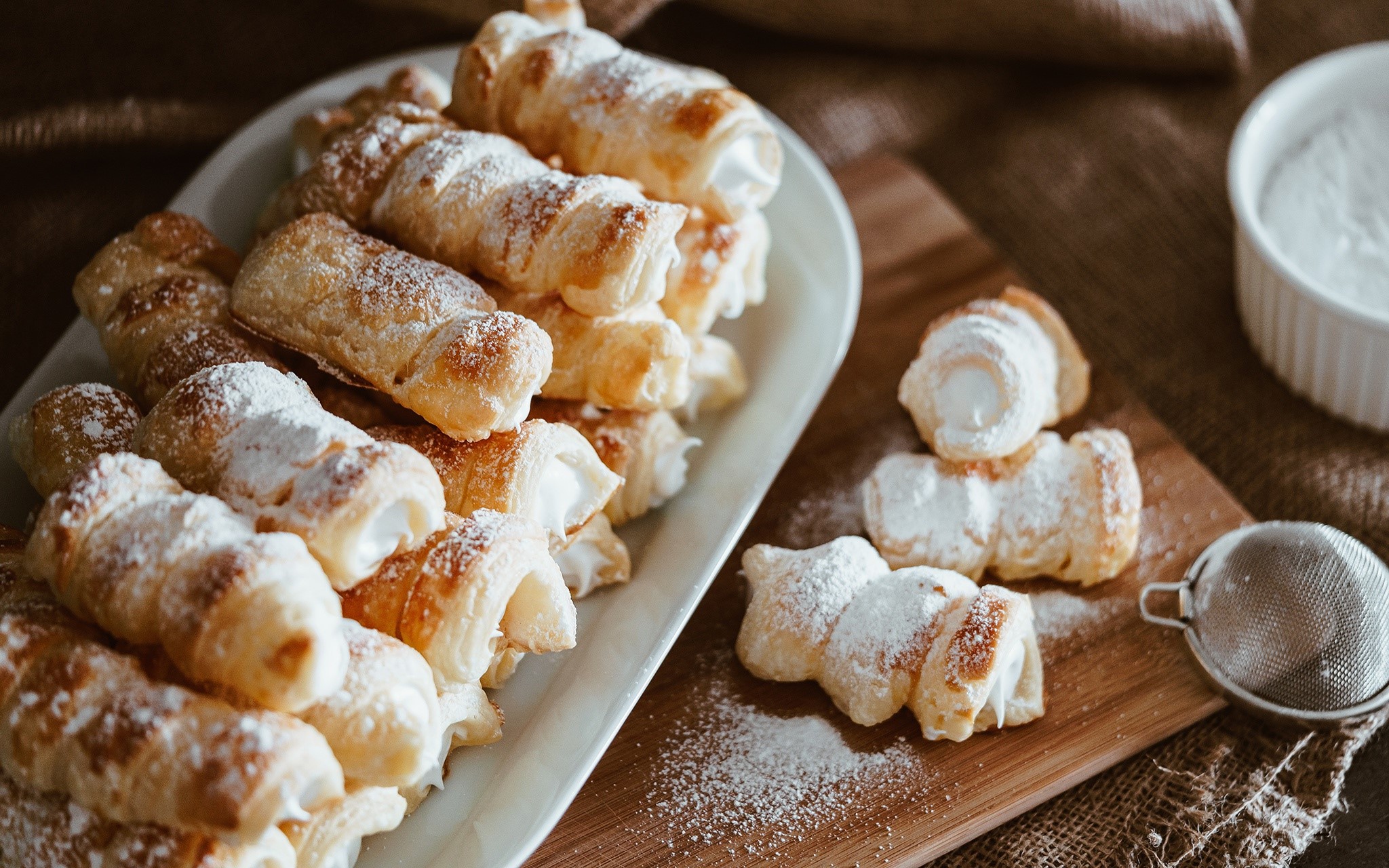 Cream-filled pastries dusted with powdered sugar on a platter HD Wallpaper