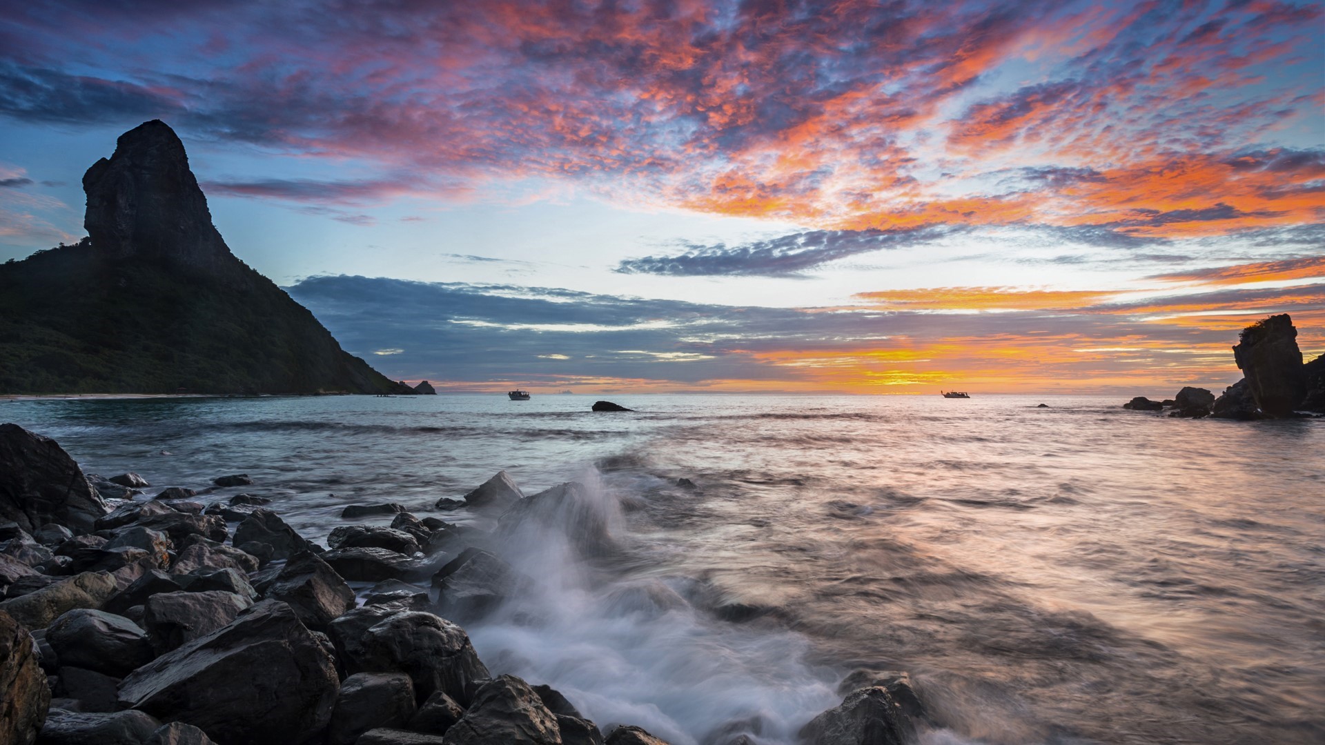 Sunset over the ocean with rocky shore and mountain HD Wallpaper
