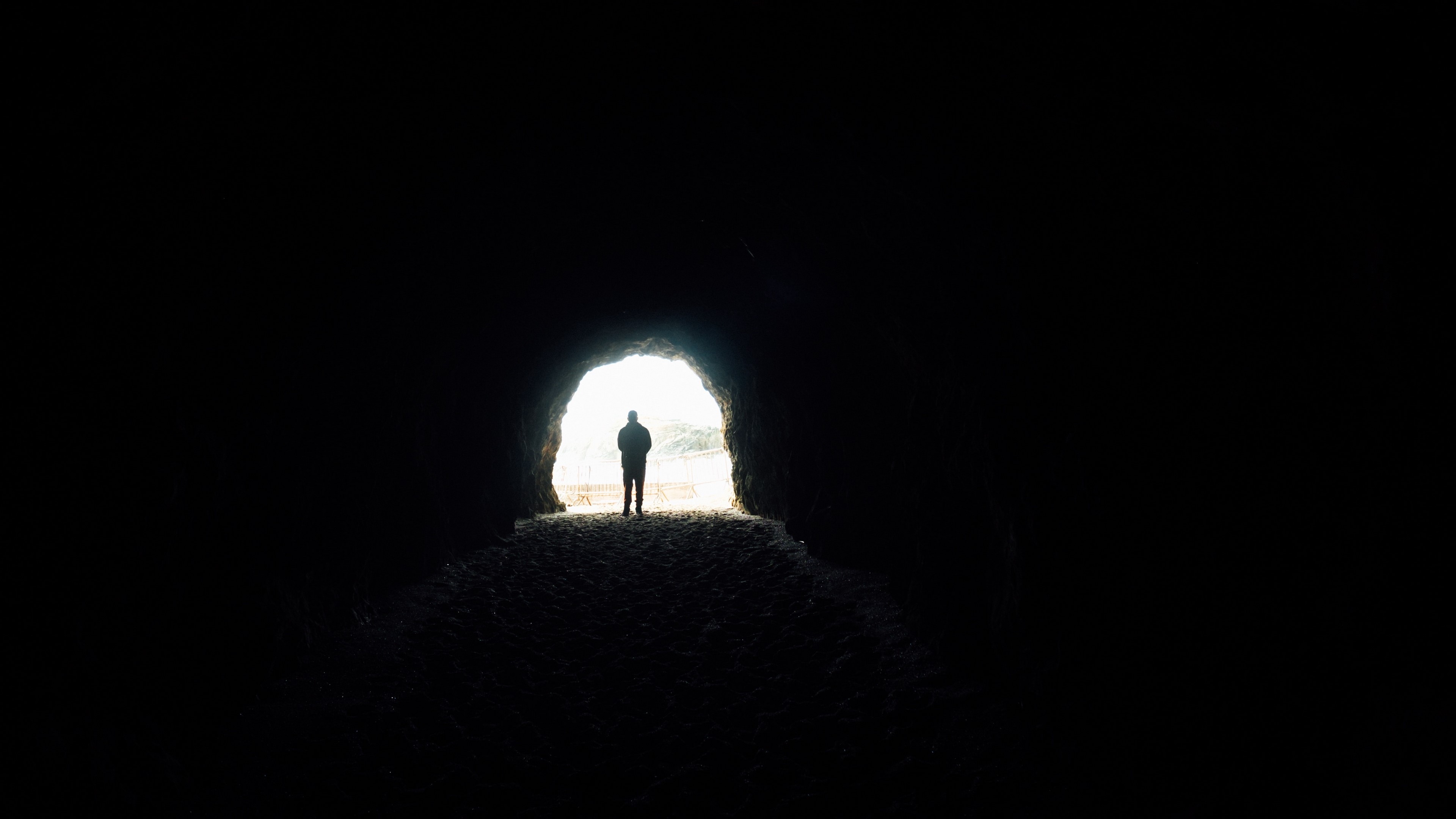 Silhouette of a person in a dark cave tunnel HD Wallpaper