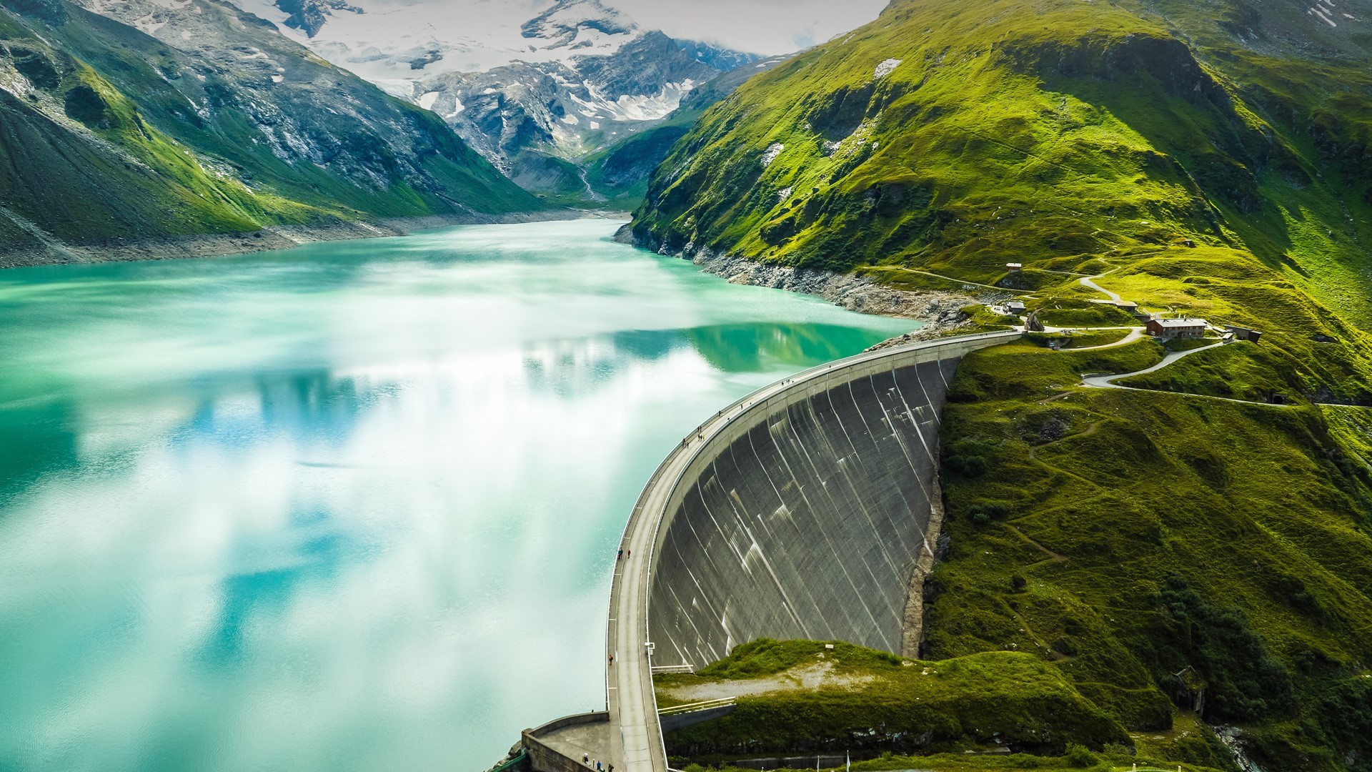 Curved dam holding back a turquoise lake in the mountains HD Wallpaper
