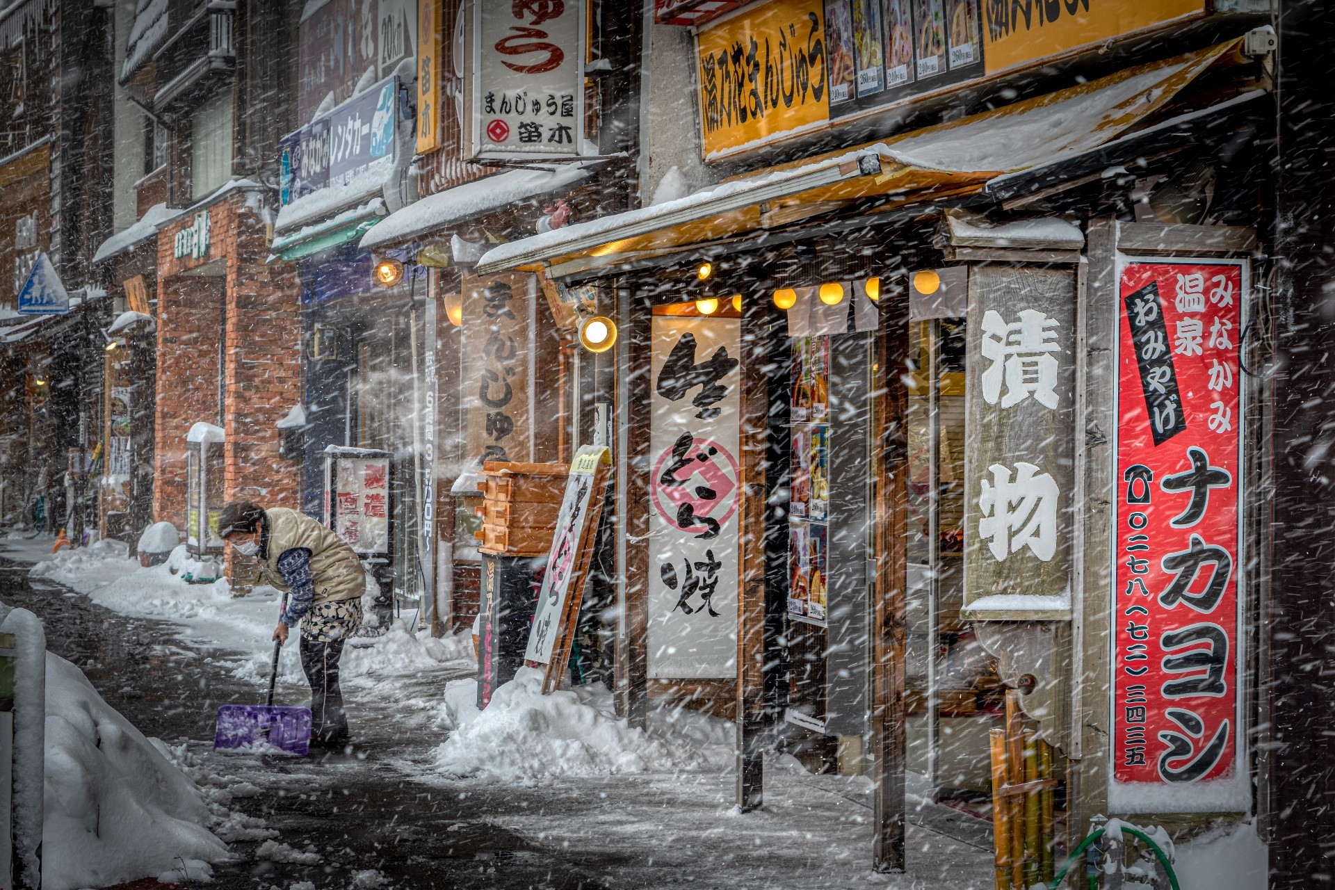 Person shoveling snow in a Japanese city during winter HD Wallpaper