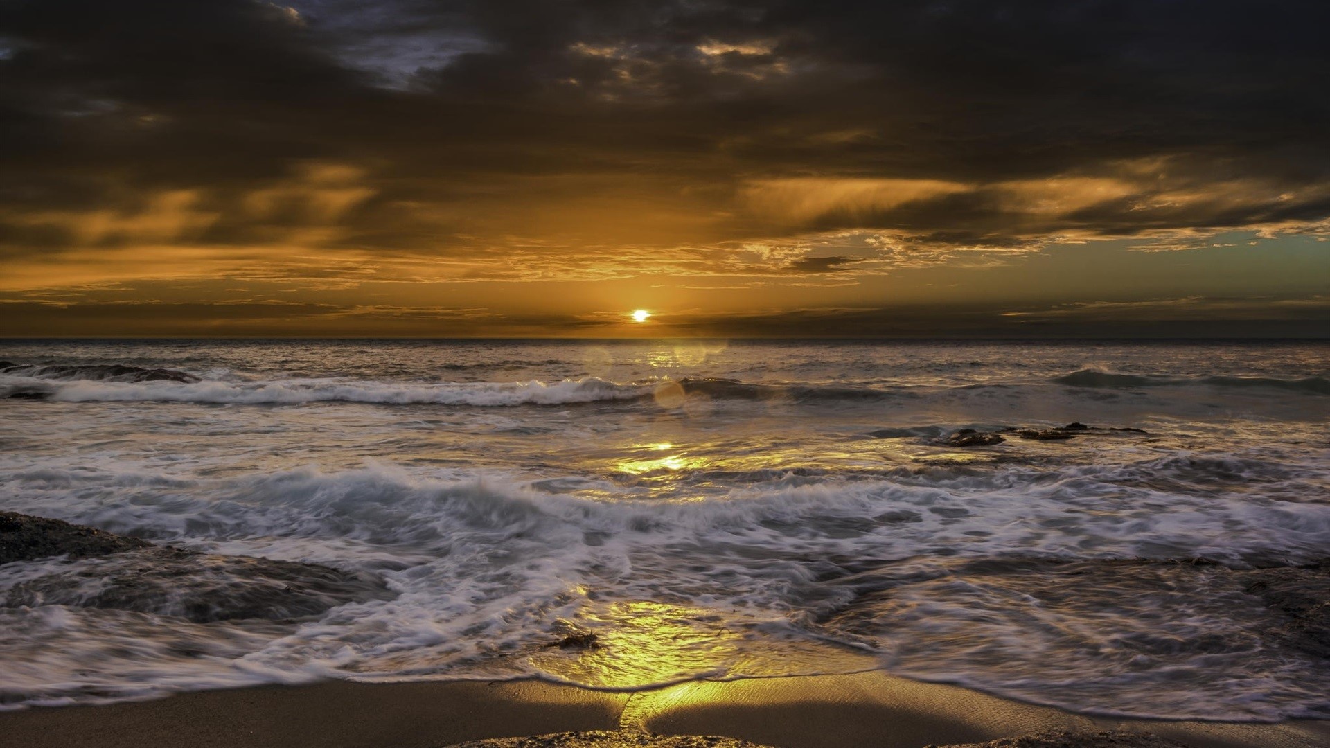 Sunset over the ocean with waves crashing on the beach HD Wallpaper