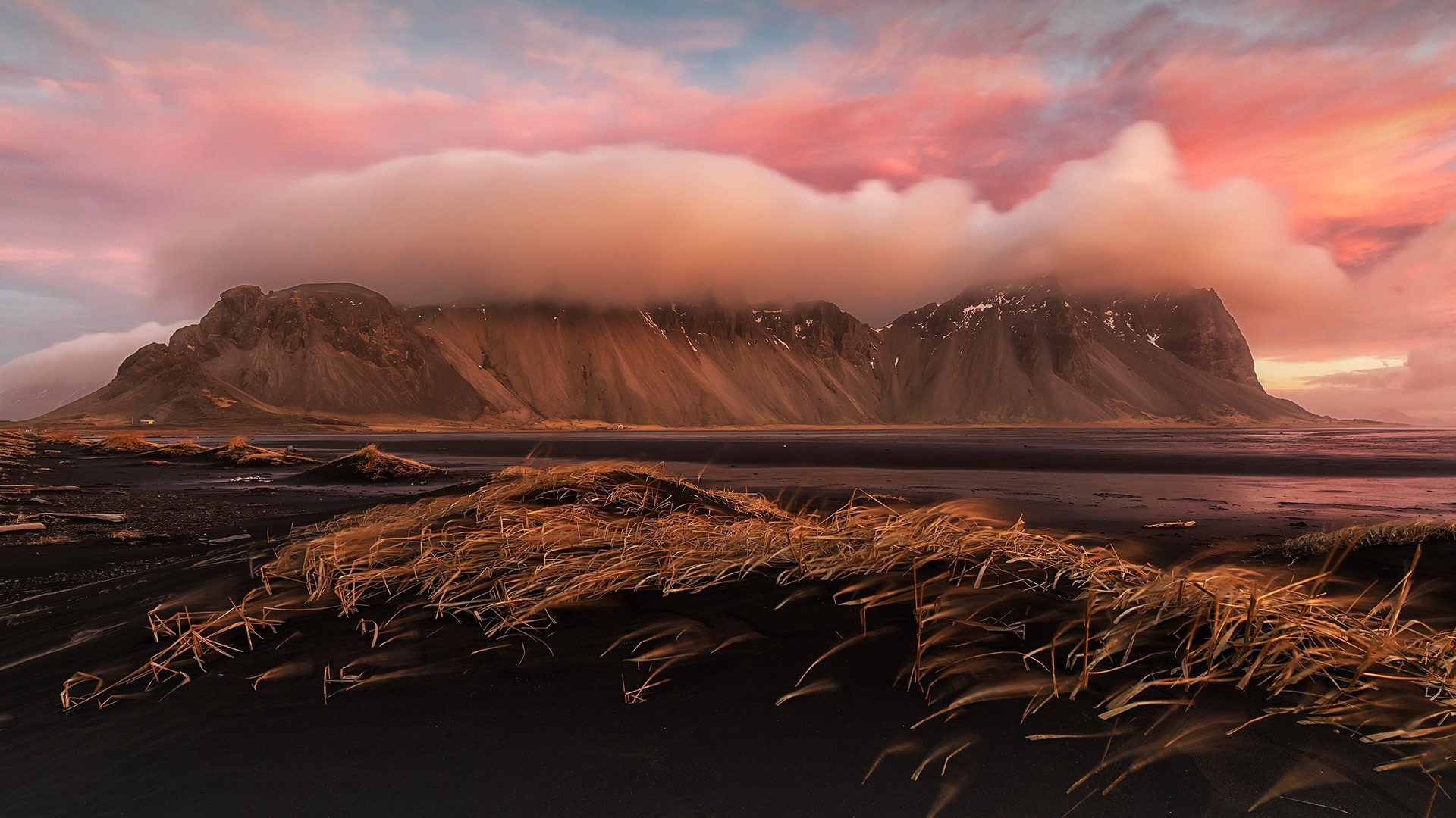 Mountains covered in clouds over black sand beach at sunset HD Wallpaper