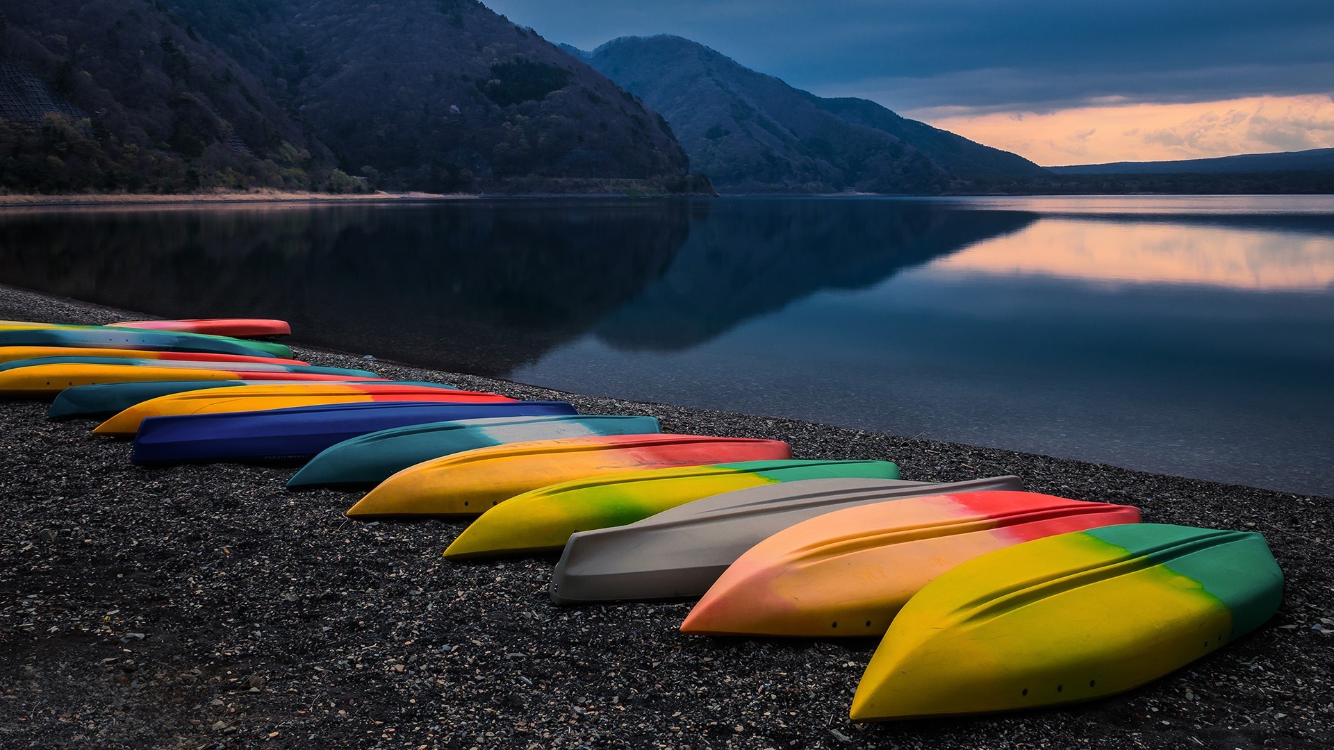 Colorful kayaks lined up on black sand beach at Lake Motosu, Japan HD Wallpaper