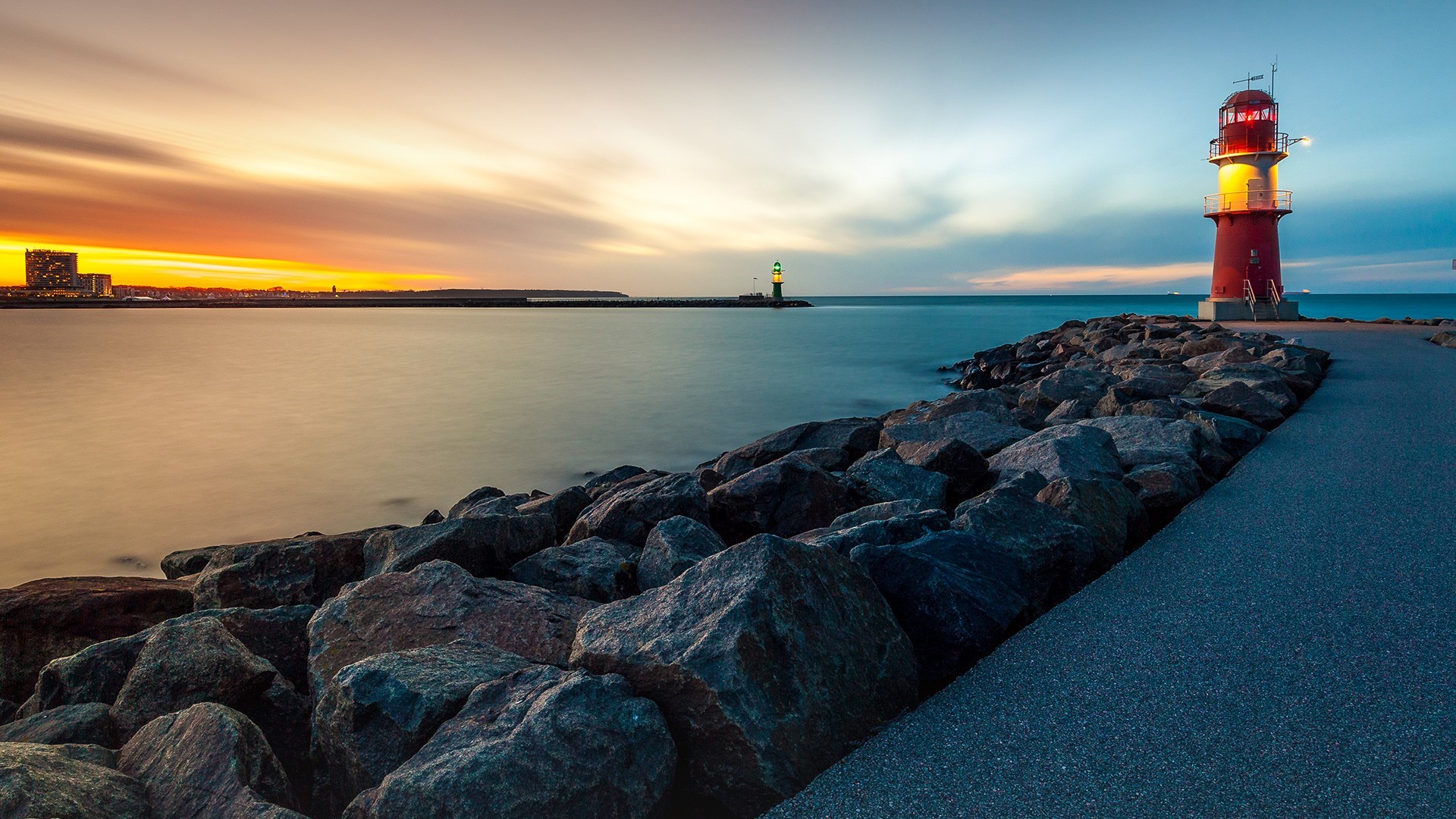 Lighthouse at sunset on a rocky shore HD Wallpaper