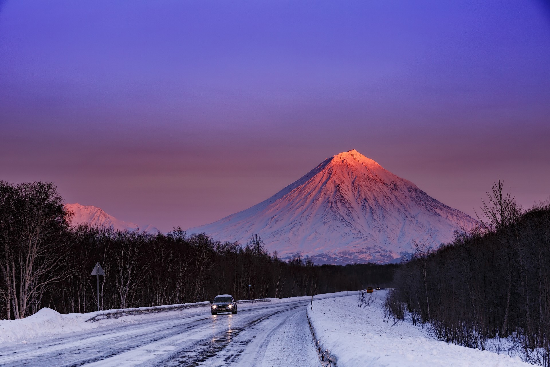 Car on snowy road with volcano at sunset HD Wallpaper