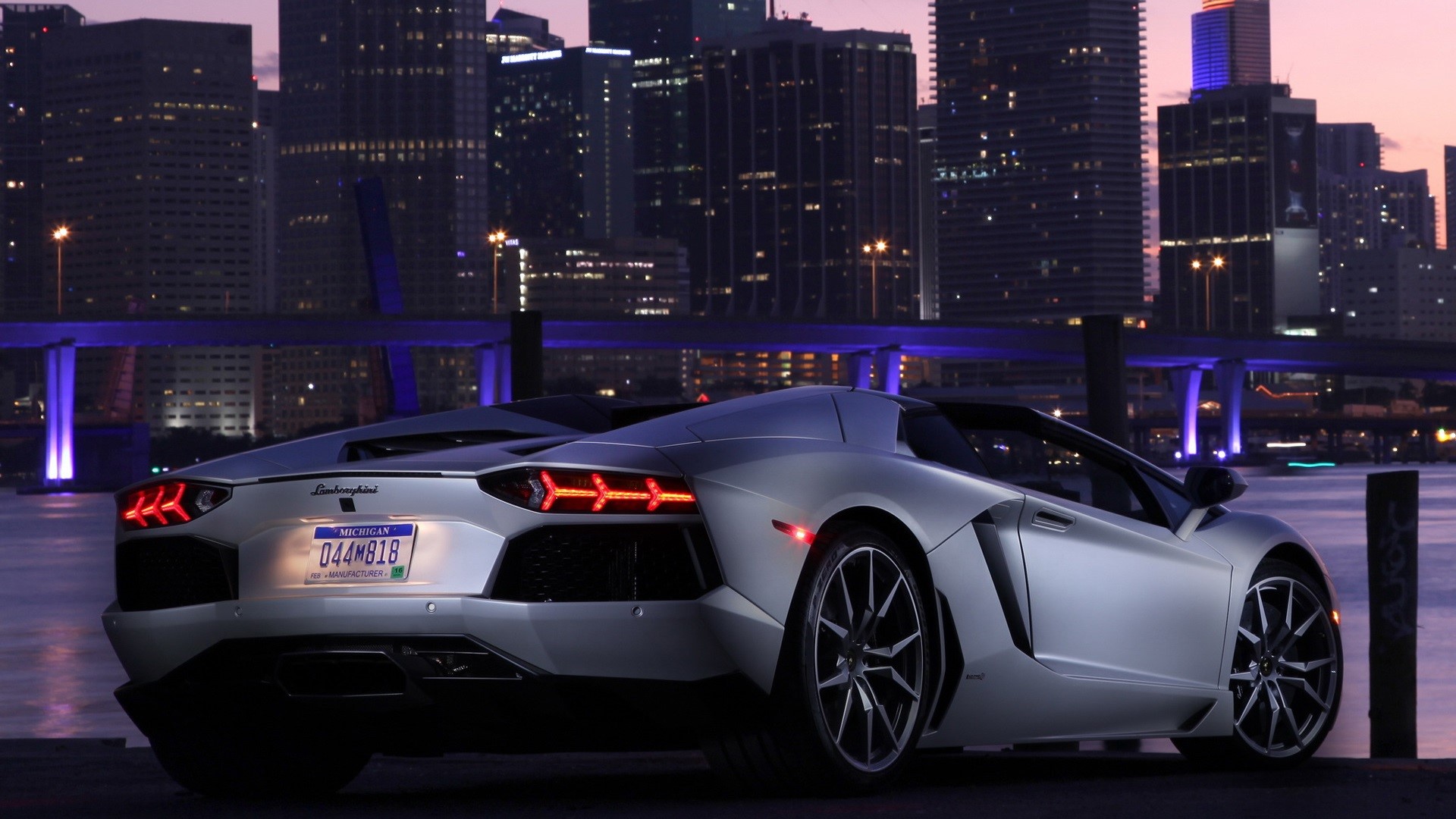 Silver Lamborghini Aventador parked by a city skyline at dusk HD Wallpaper