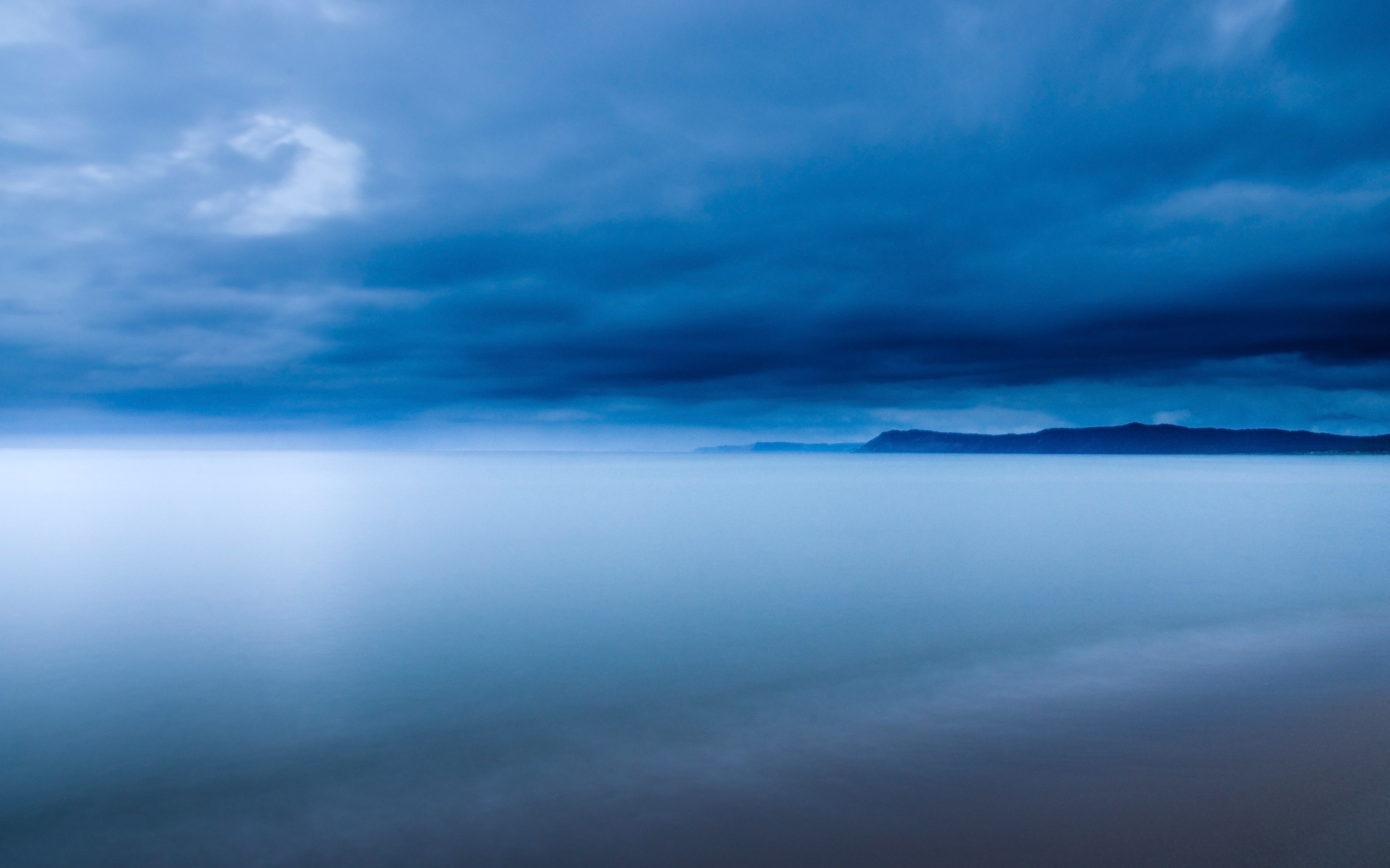 Calm ocean under a cloudy sky with distant land HD Wallpaper
