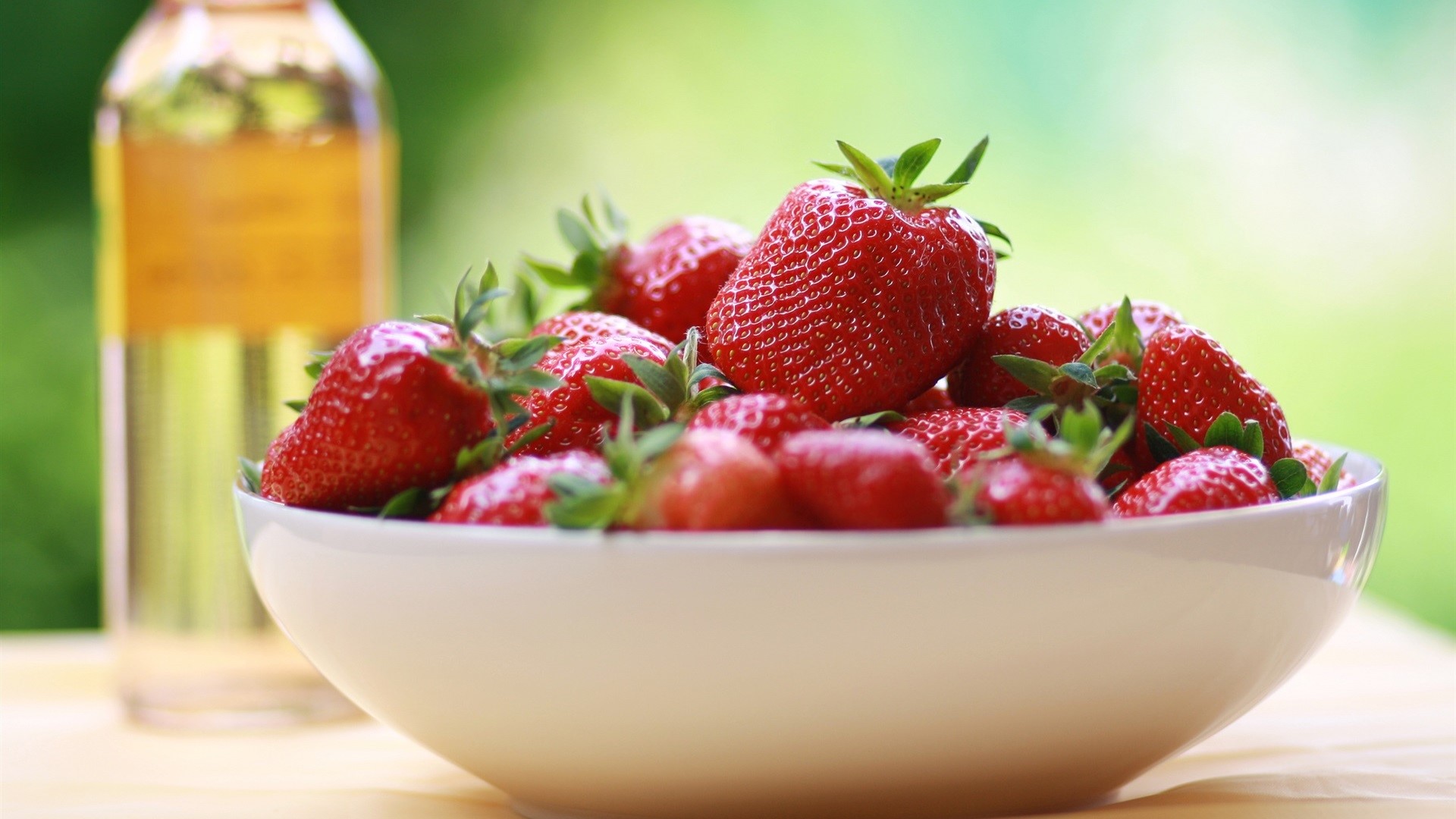 Bowl of fresh strawberries next to a bottle of liquid HD Wallpaper