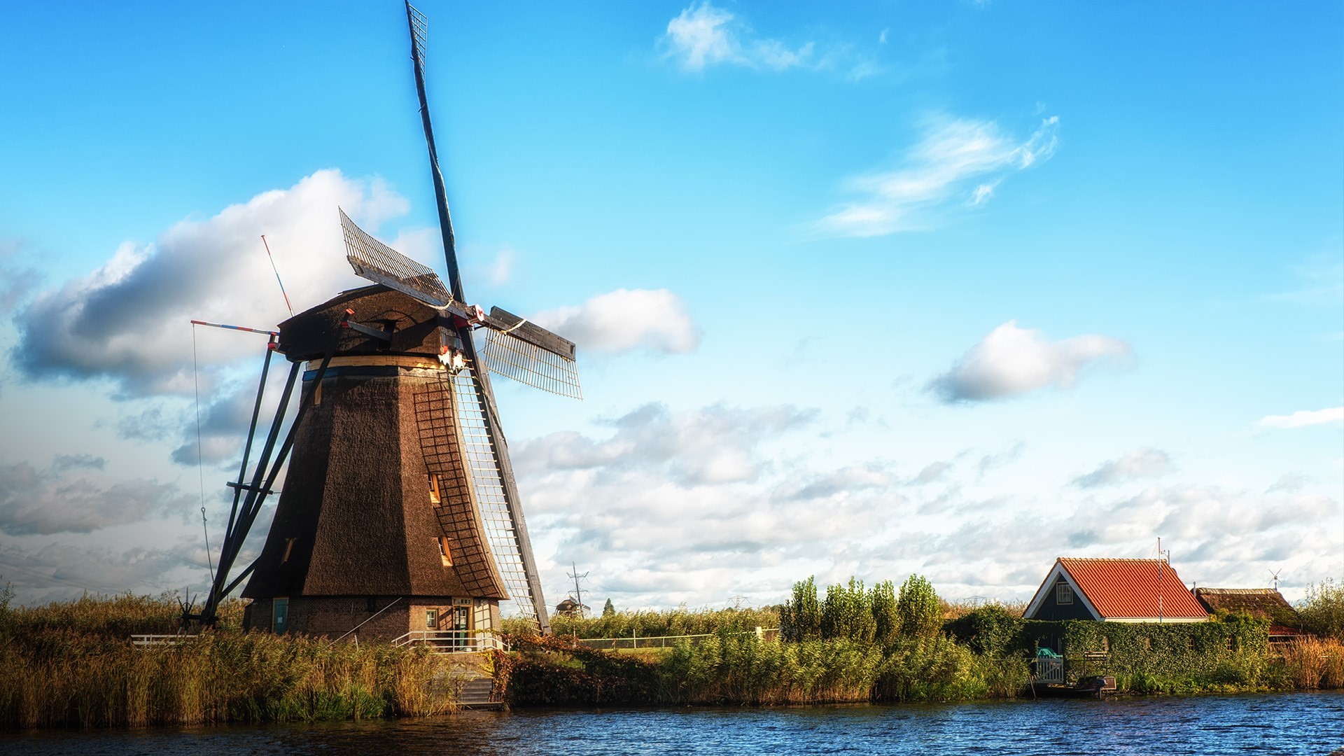 Dutch windmill and house by a canal under a cloudy sky HD Wallpaper