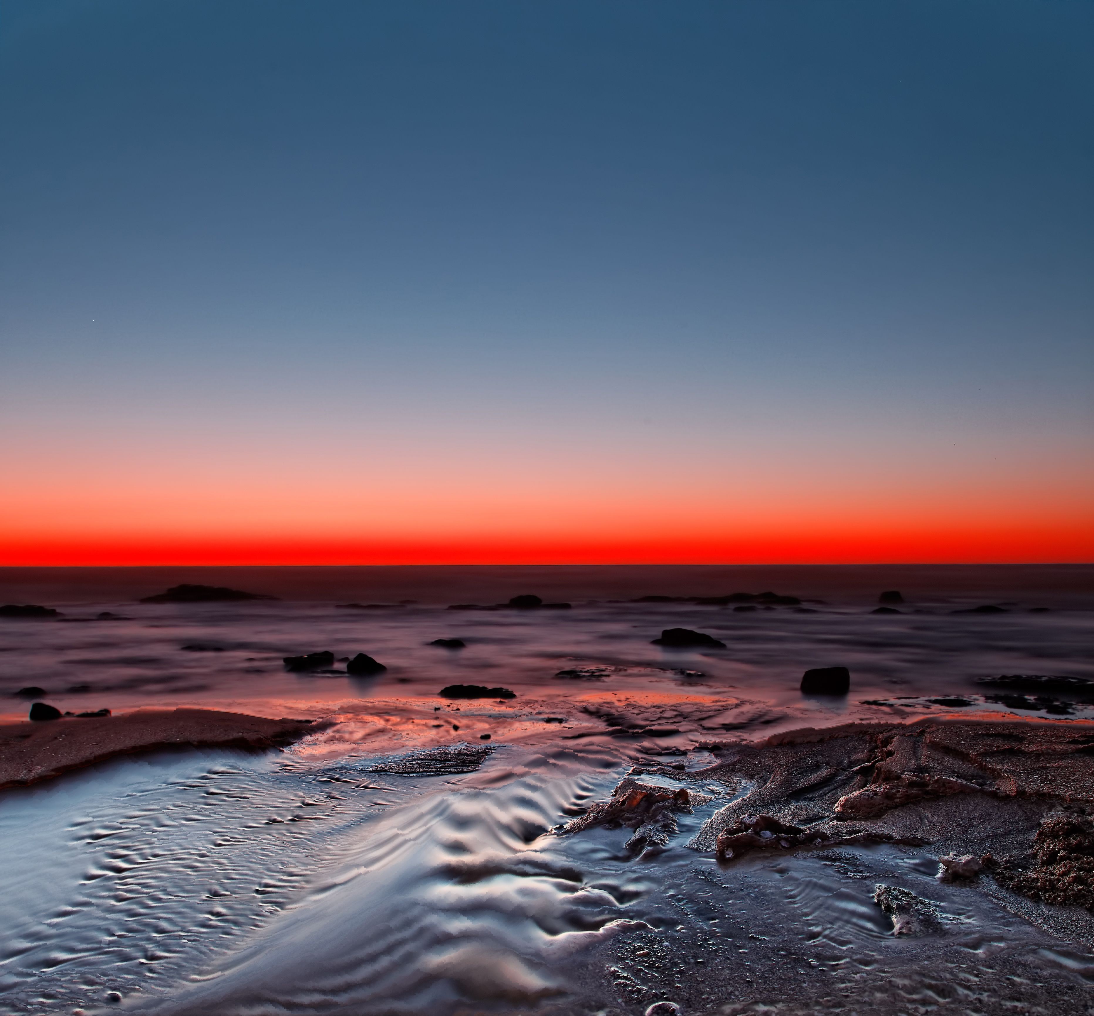 Sunset over the ocean with rocks and sand HD Wallpaper