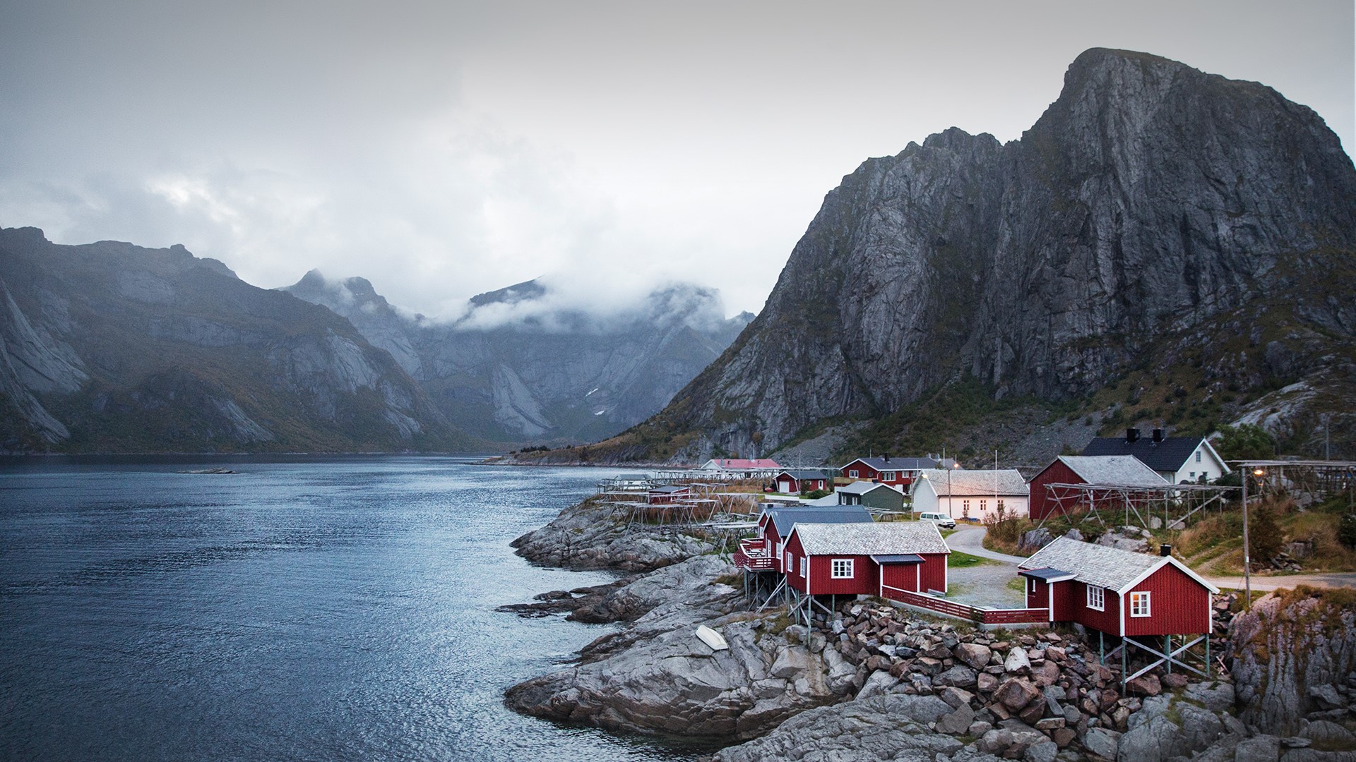Red houses on rocky shore with mountains and water HD Wallpaper