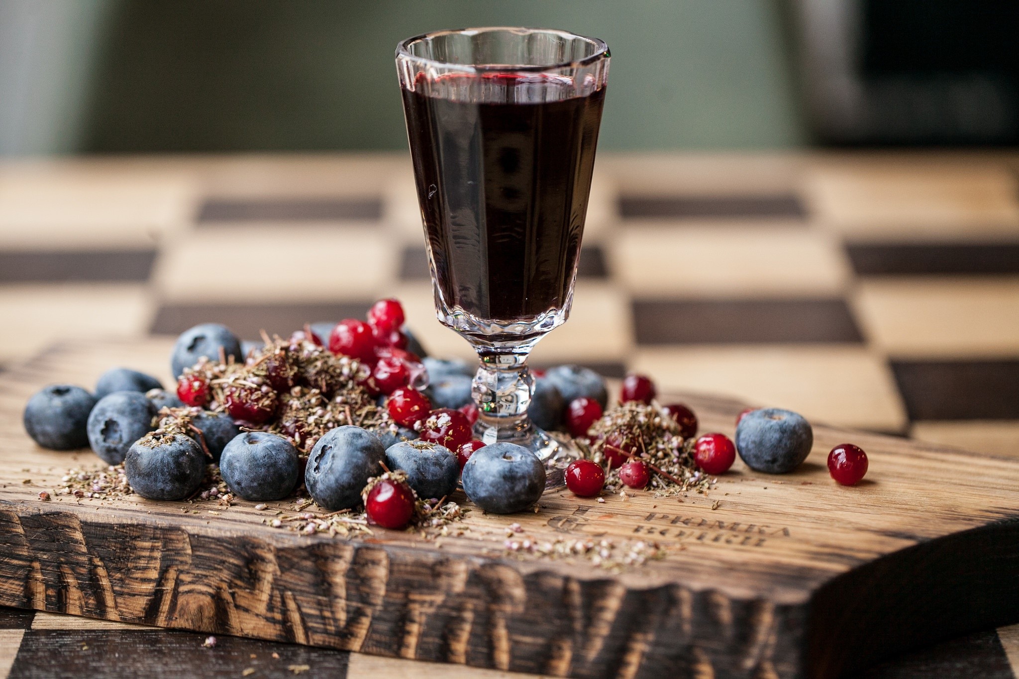 Glass of dark liquid with blueberries and cranberries on a wooden board HD Wallpaper