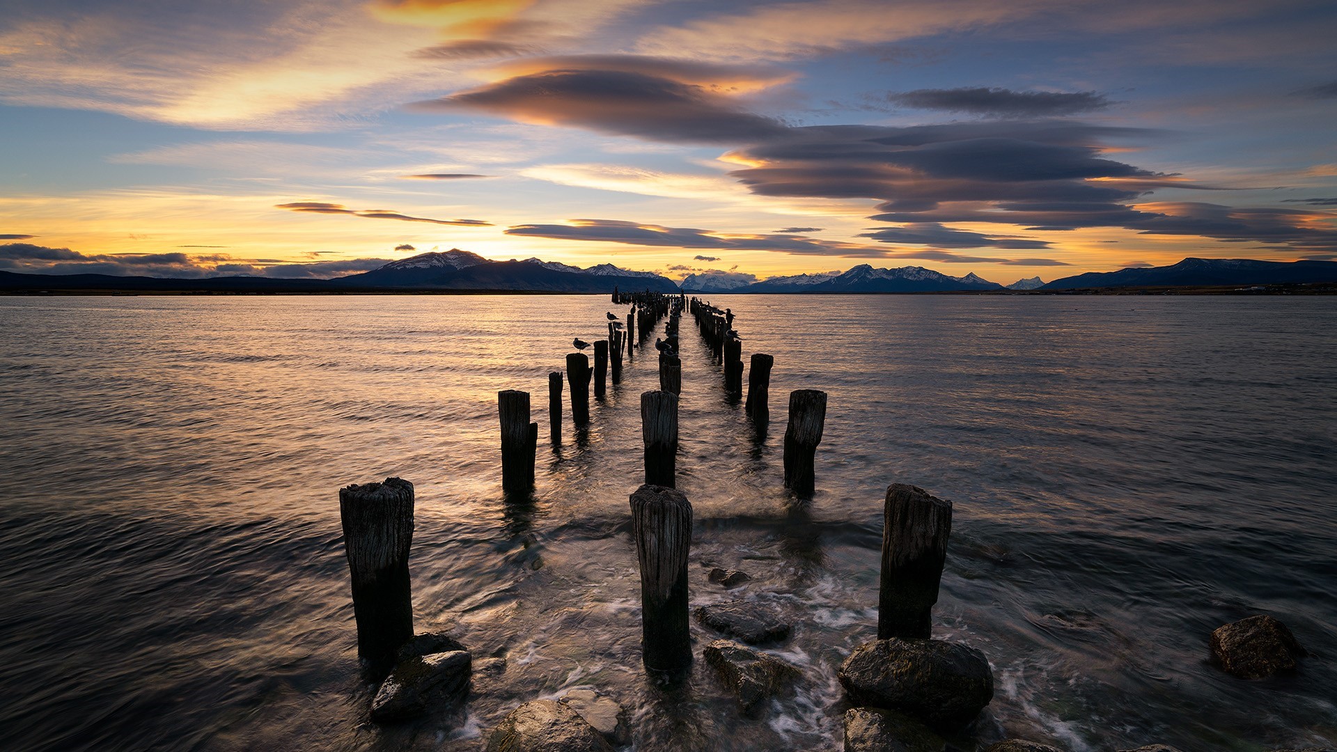 Old pier pilings in the water at sunset with mountains HD Wallpaper