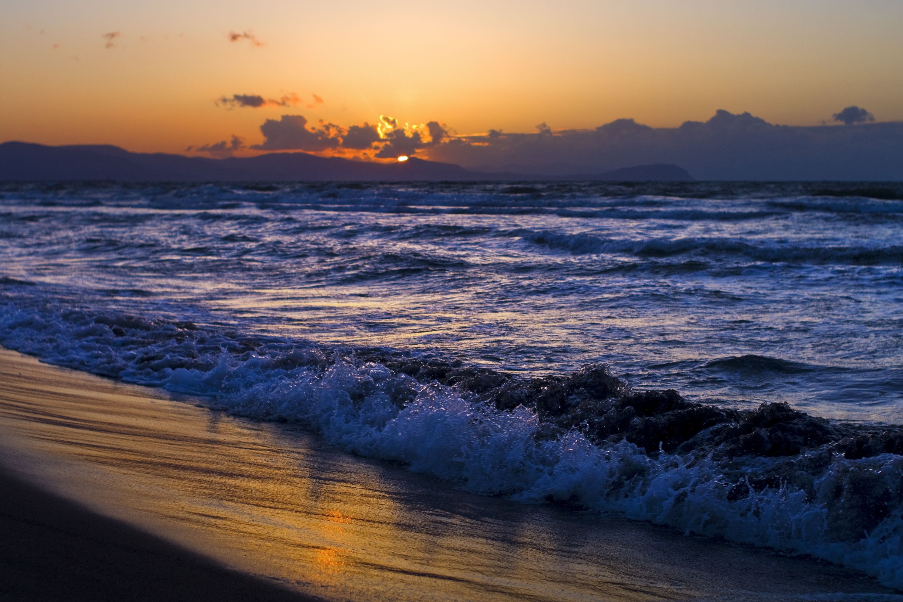 Sunset over the ocean with waves crashing on the beach HD Wallpaper