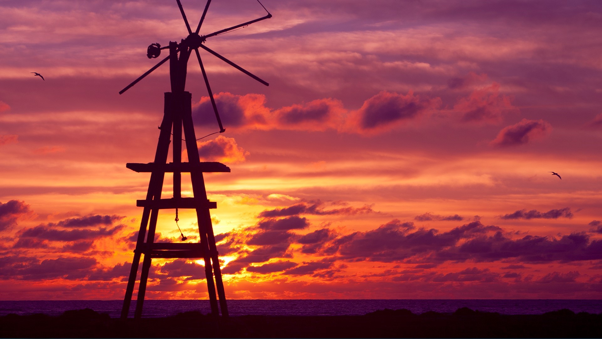 Silhouette of a windmill against a colorful sunset sky over the sea HD Wallpaper
