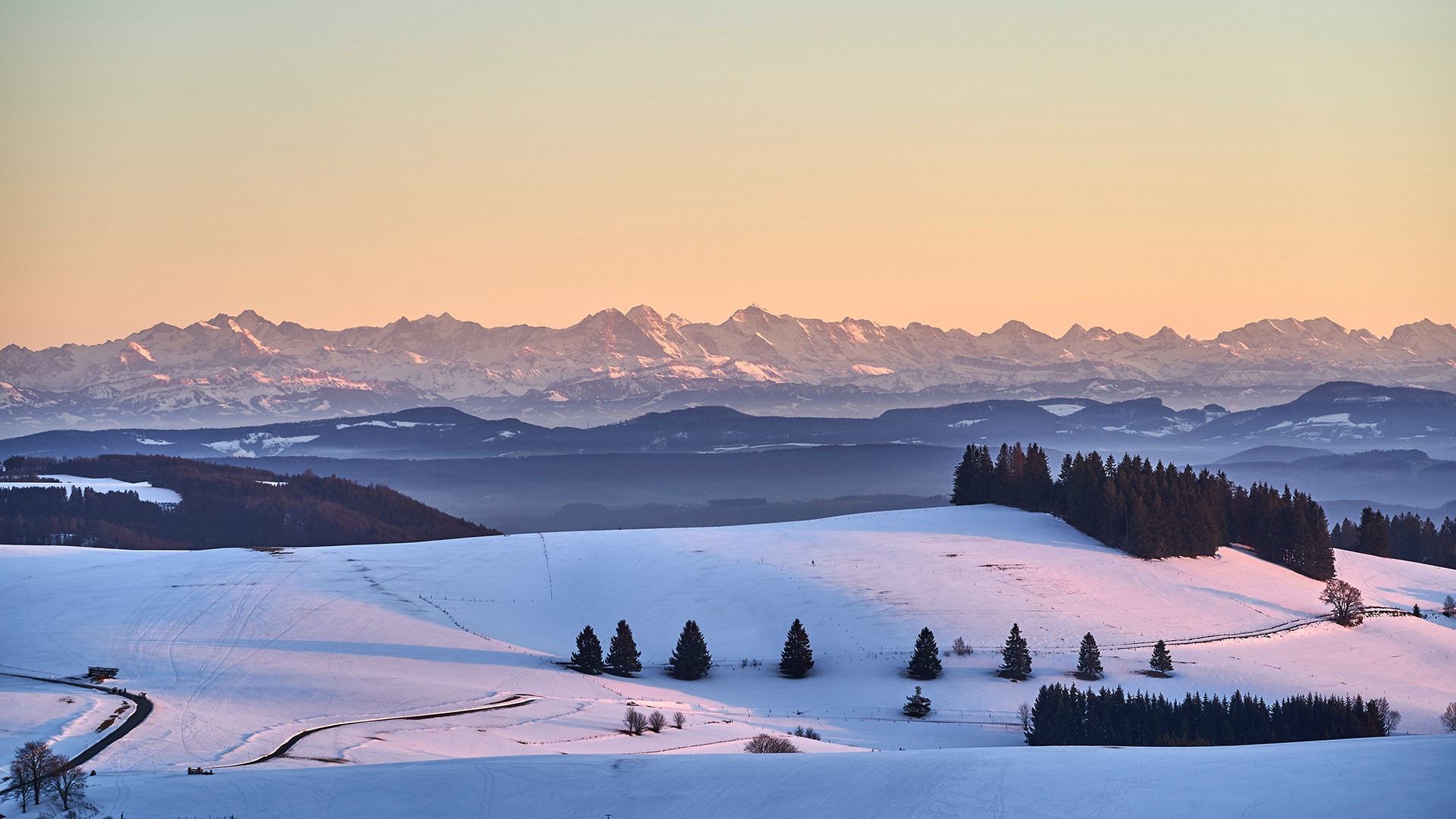 Snowy mountain landscape with trees and road at sunset HD Wallpaper