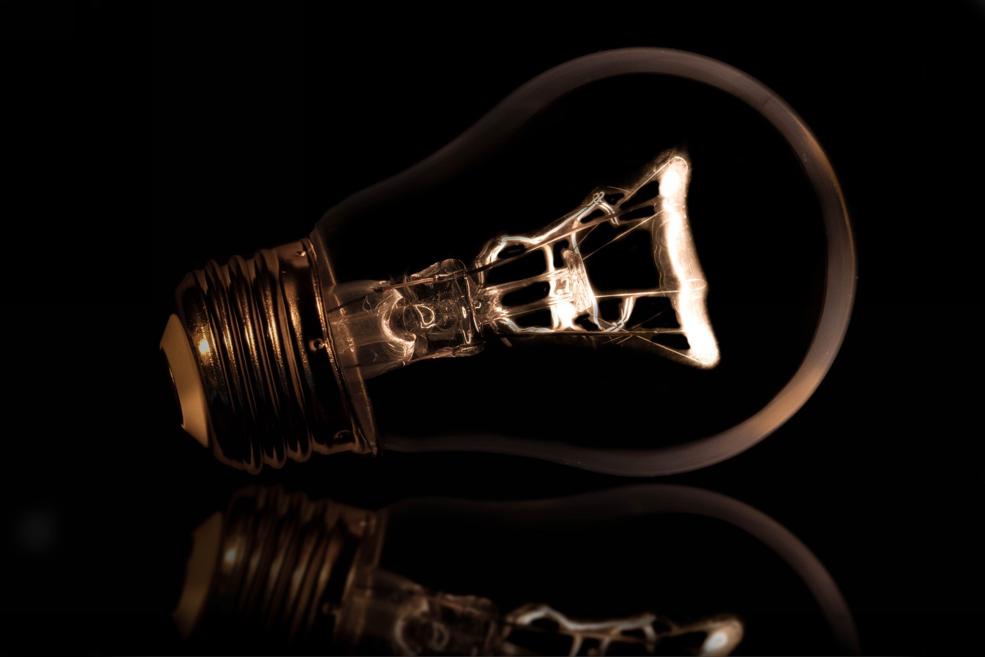 Close-up of a lit incandescent lightbulb on a dark surface HD Wallpaper