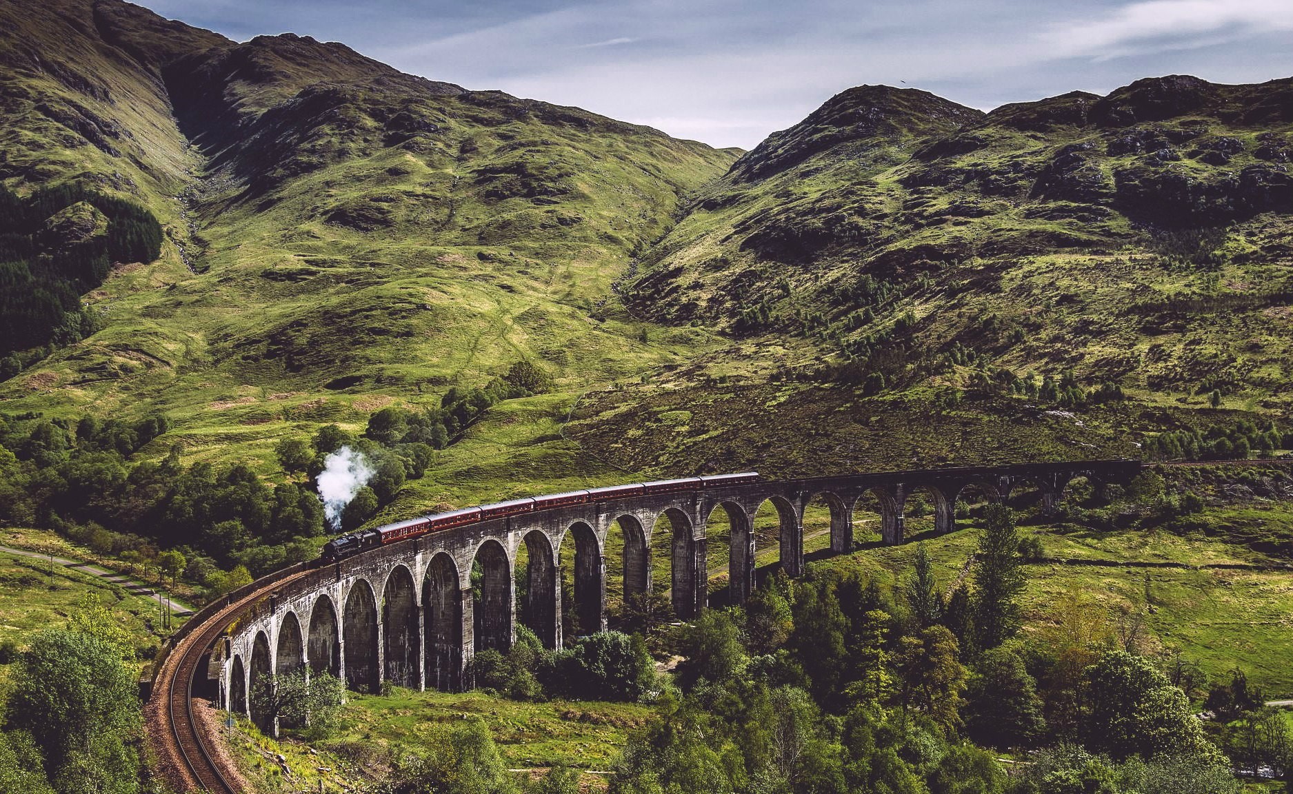 Train crossing a viaduct in a mountainous landscape HD Wallpaper