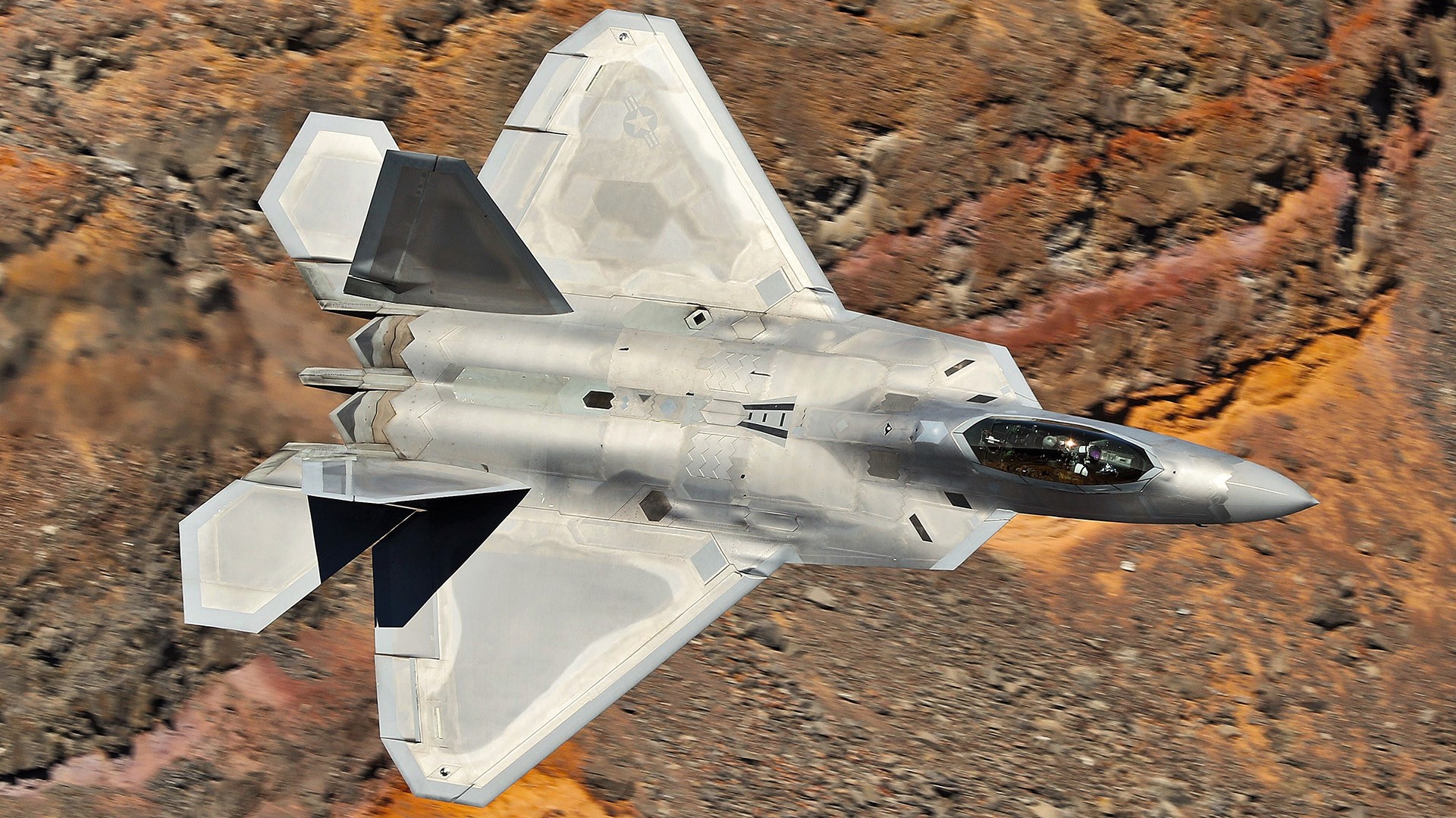 F-22 Raptor jet fighter flying over rocky terrain HD Wallpaper