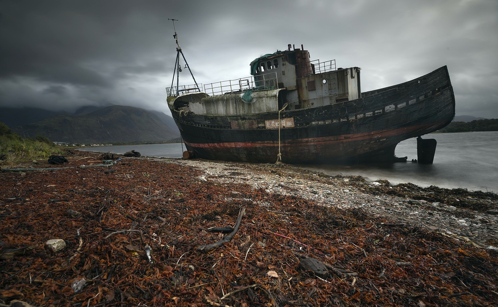 Abandoned shipwreck on a rocky shore under stormy skies HD Wallpaper