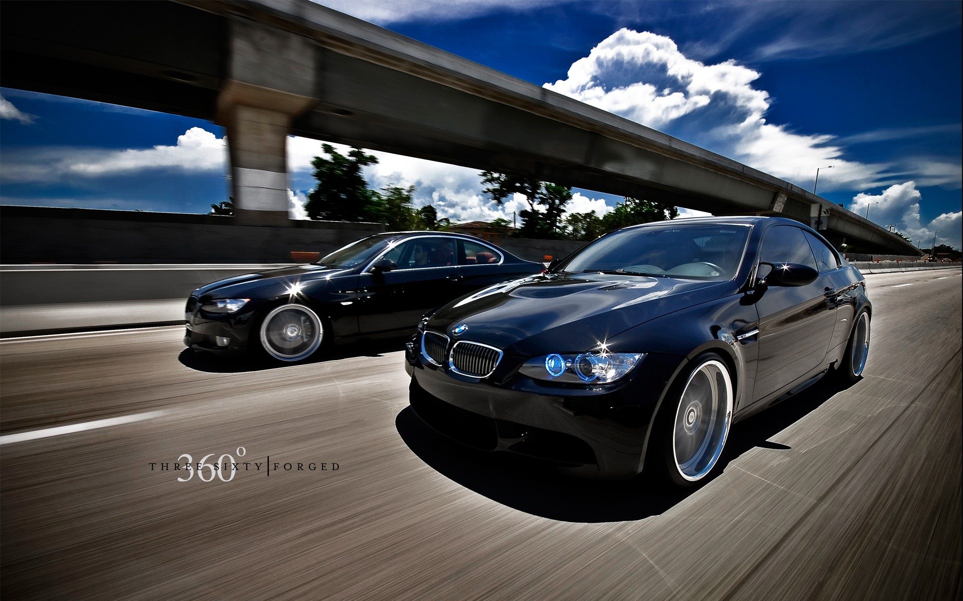 Two black BMWs driving on a highway under a bridge HD Wallpaper