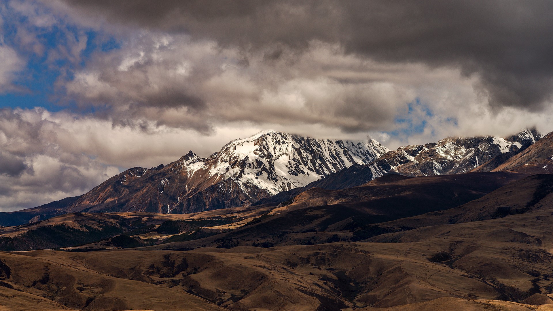 Snow-capped mountains under dramatic clouds in Sichuan HD Wallpaper