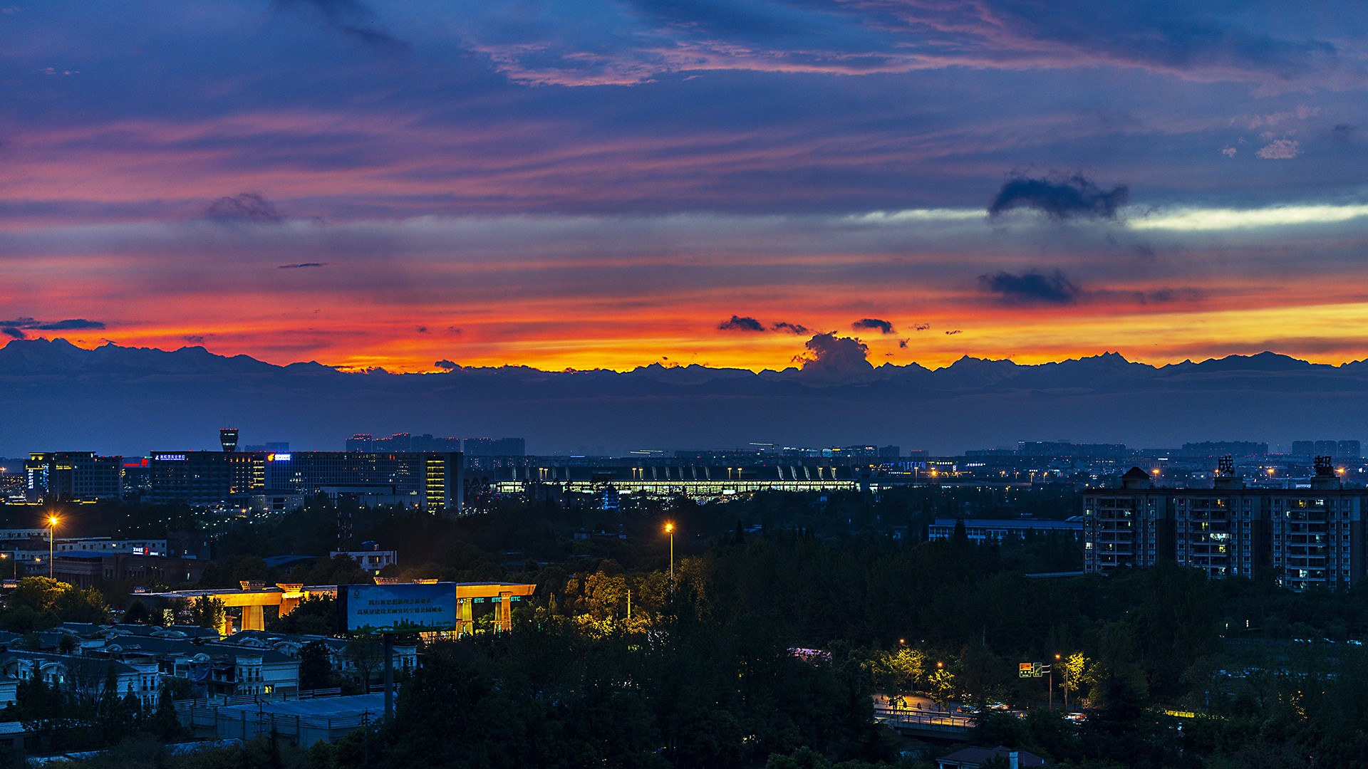 Cityscape at sunset with mountains in the background HD Wallpaper