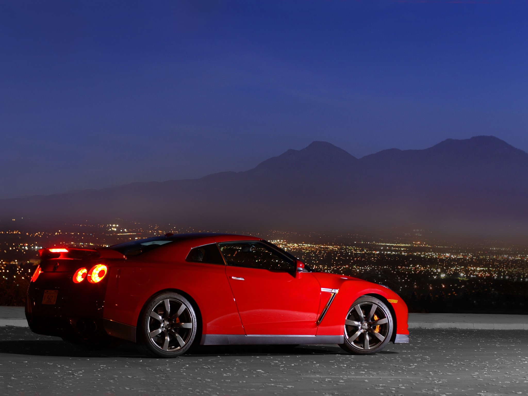 Red Nissan GTR parked at night overlooking city lights HD Wallpaper