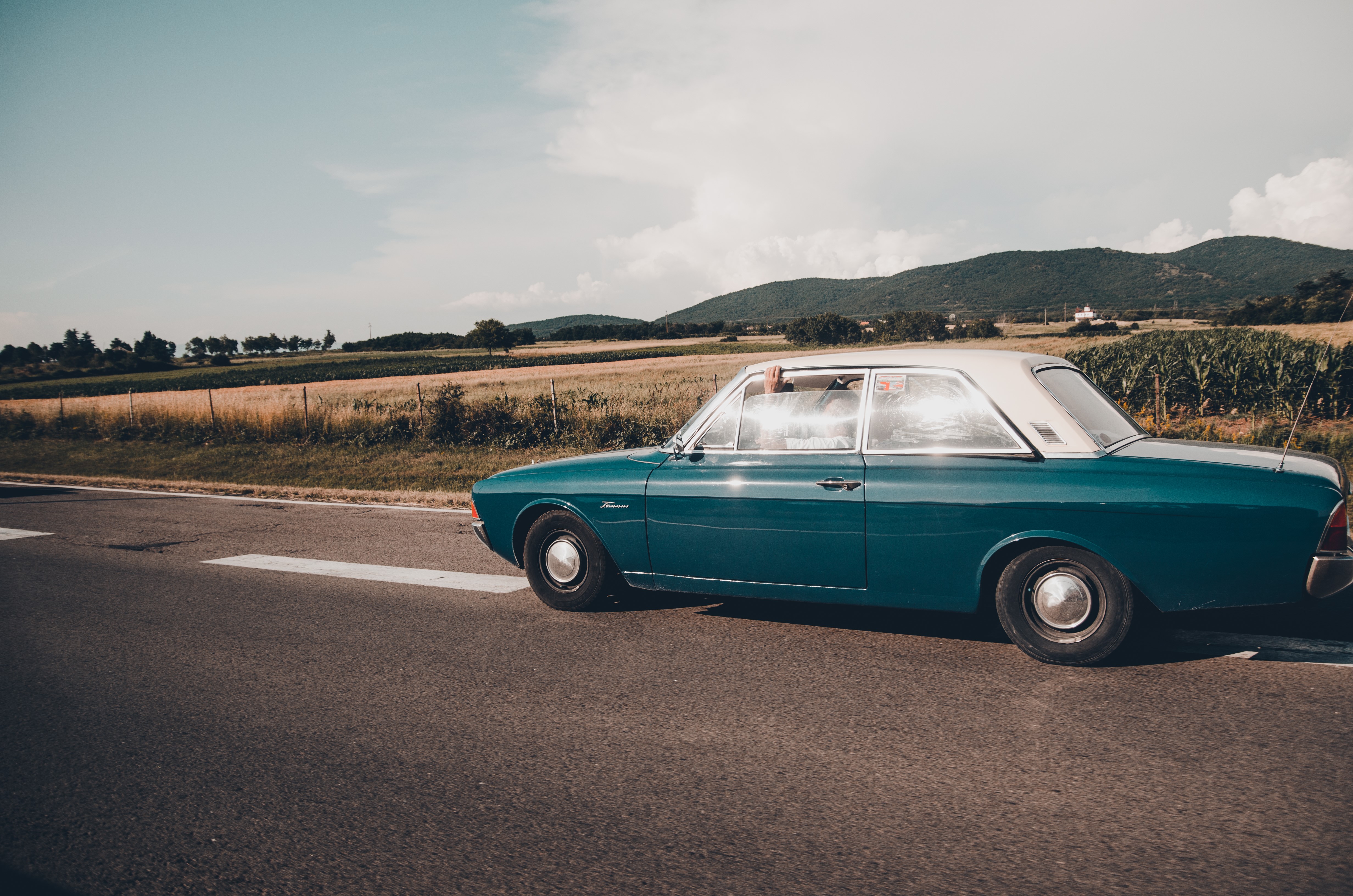 Blue vintage car driving on a road with fields and mountains HD Wallpaper