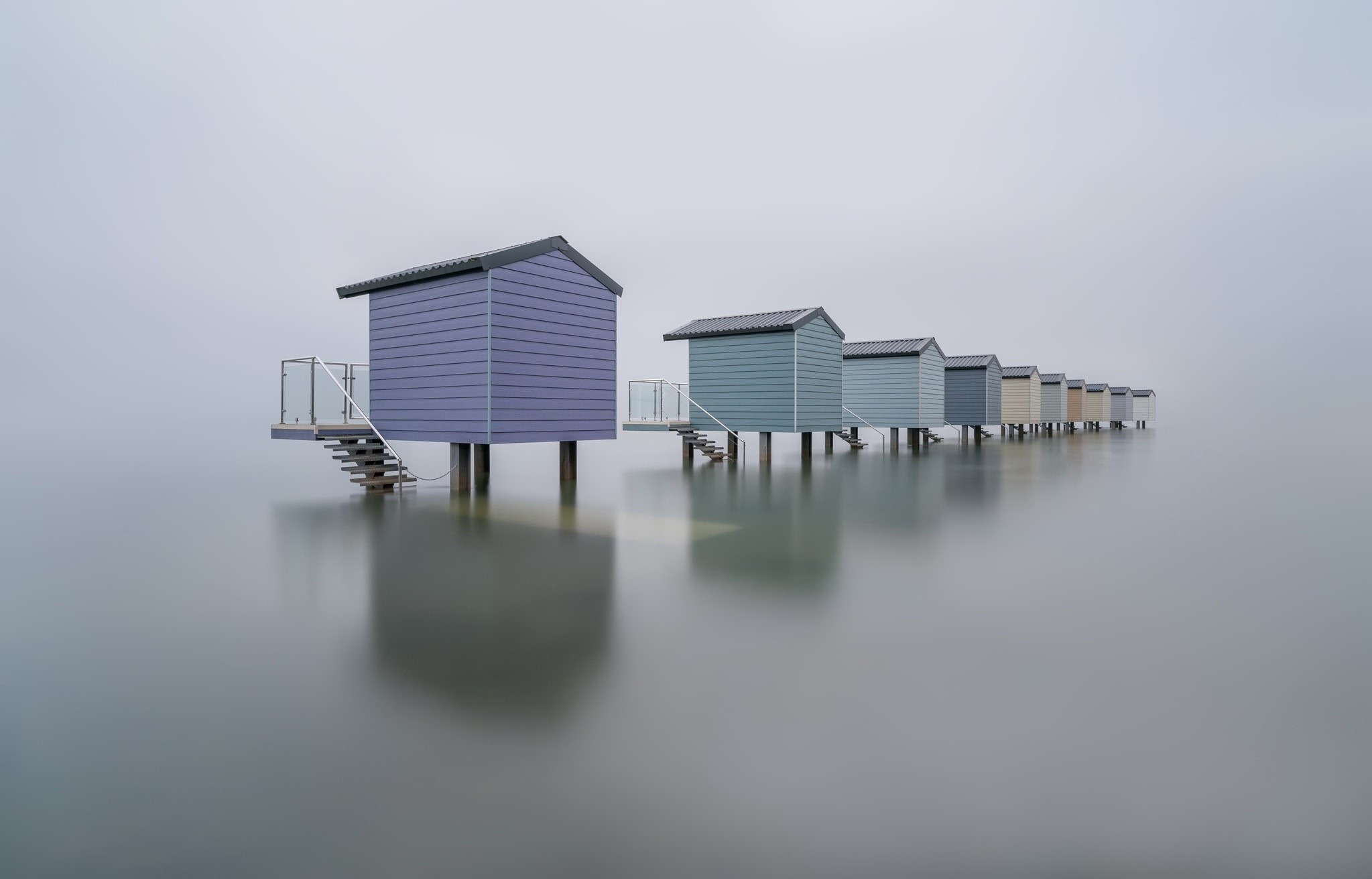 Row of colorful beach huts on stilts in mist HD Wallpaper